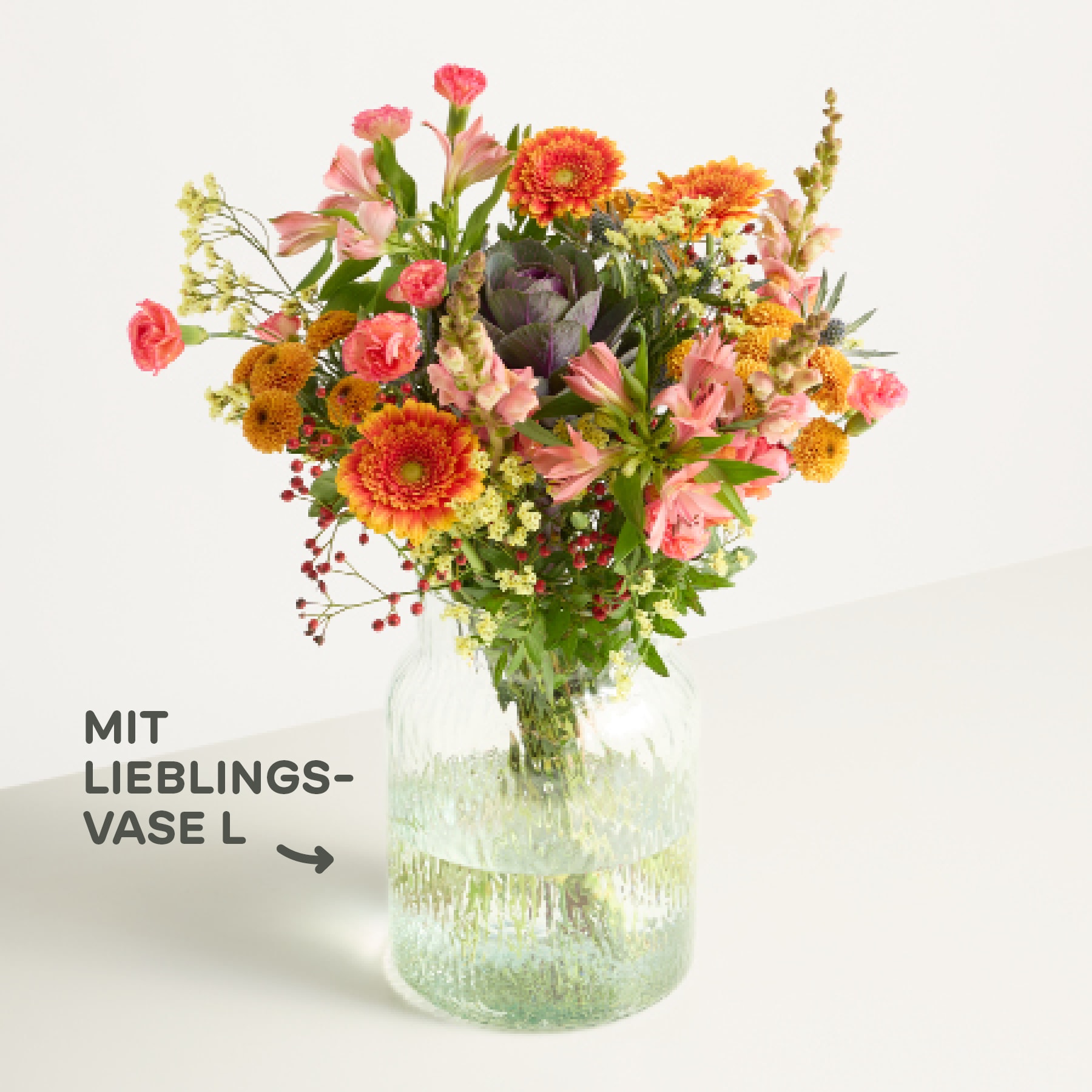 Ein lebendiger Strauß bunter Blumen, darunter Sonnenblumen, Nelken und andere Blüten, wird in einer Glasvase vor einem schlichten weißen Hintergrund präsentiert.