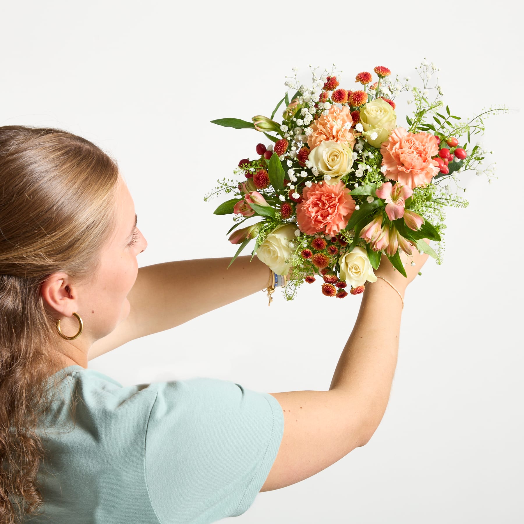 Ein lebendiger Strauß bunter Blumen, darunter rosa und orange Dahlien, gelbe Rosen und lila Gänseblümchen, vor einem hellen Hintergrund.