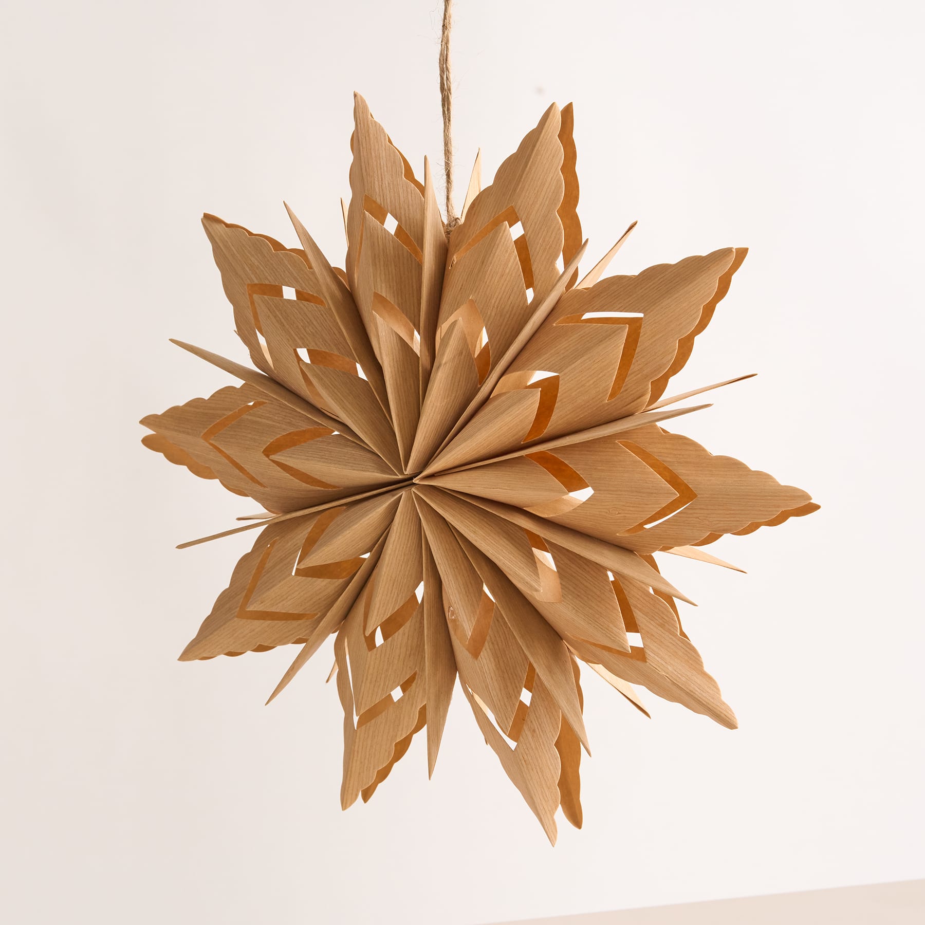 Ein zartes, weißes Schneeflockenornament aus Papier hängt vor einem schlichten, blassen Hintergrund.