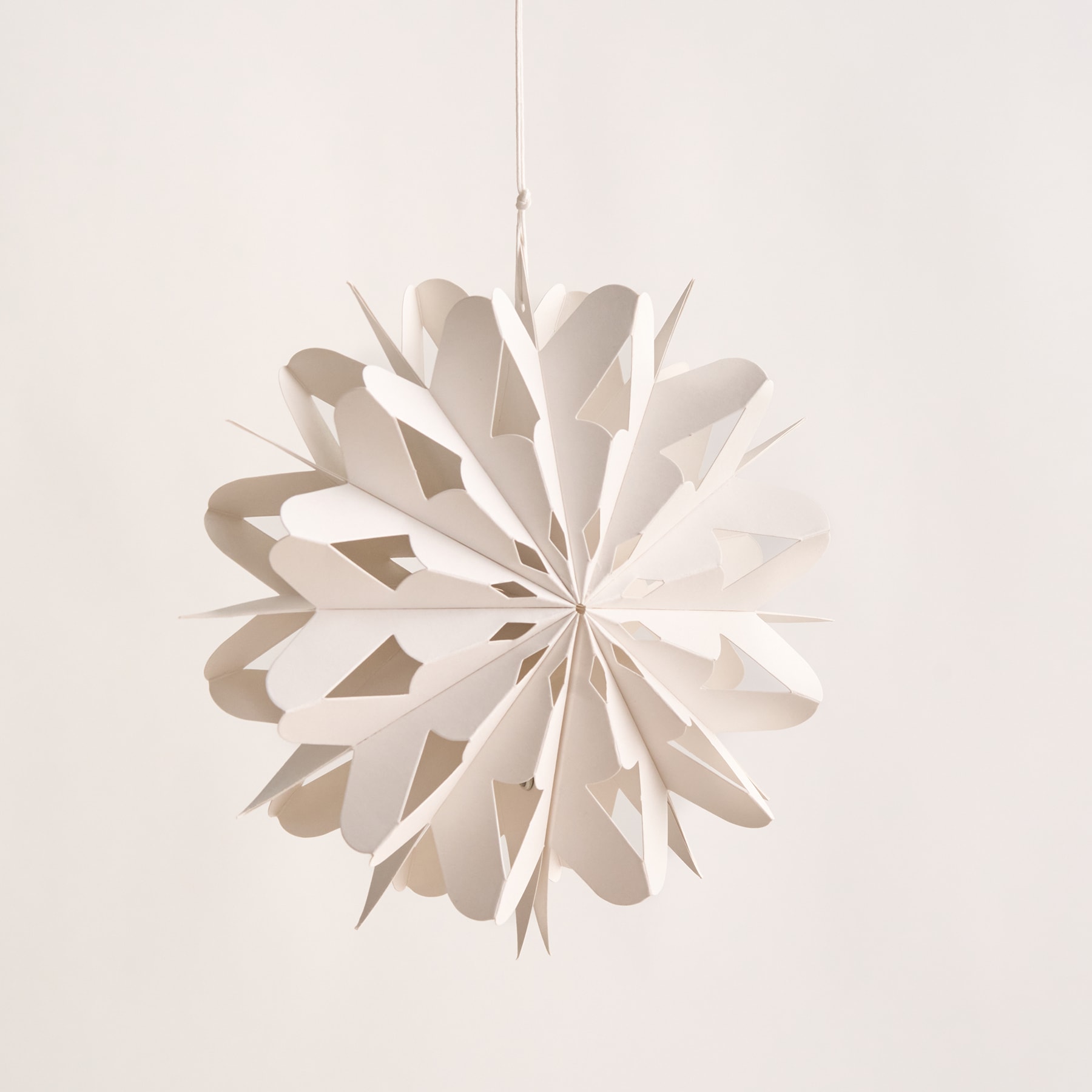 Ein zartes, weißes Schneeflockenornament aus Papier hängt vor einem schlichten, blassen Hintergrund.
