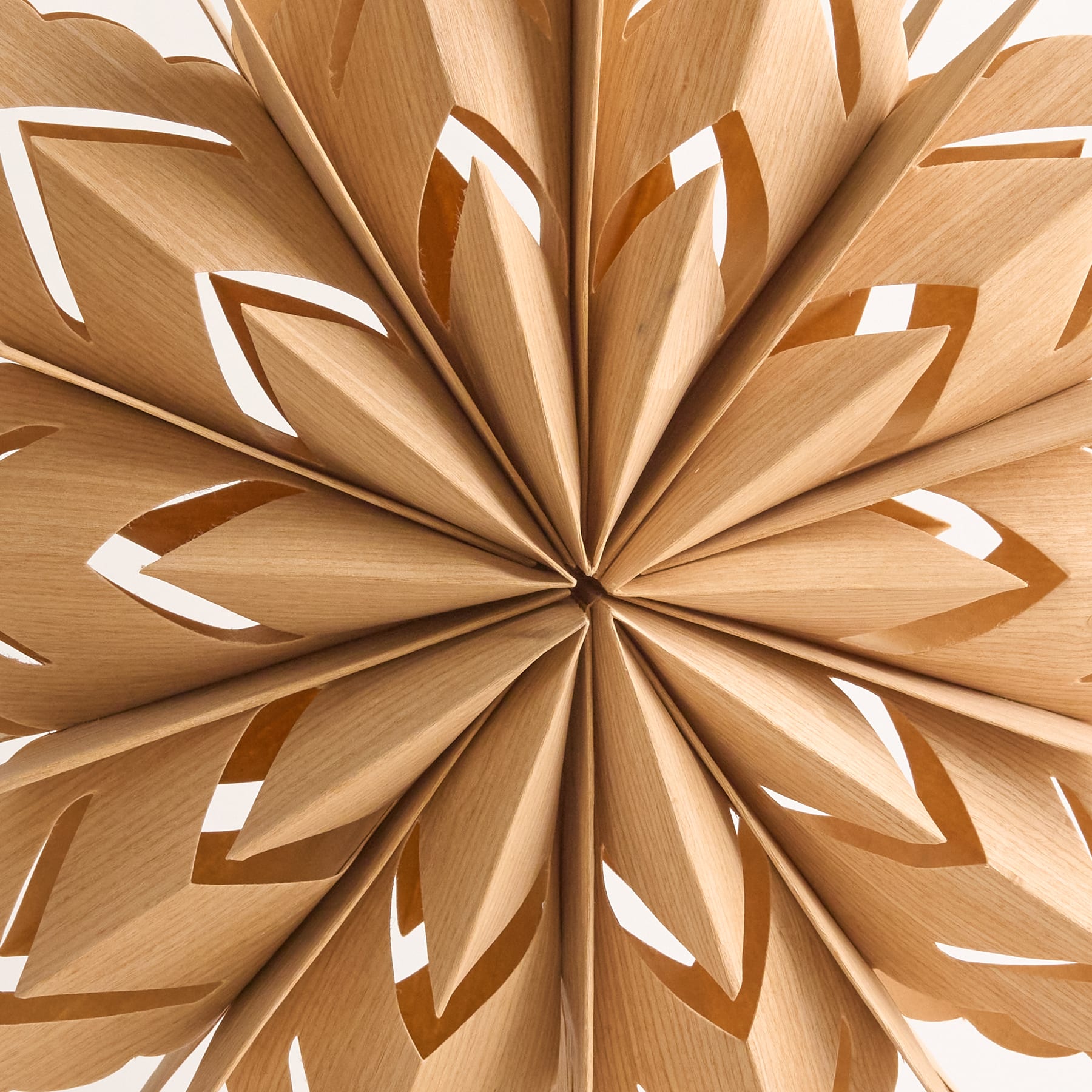 Eine zarte Schneeflockendekoration aus weißem Papier hängt vor einem schlichten weißen Hintergrund an einer Vase mit kahlen Ästen.