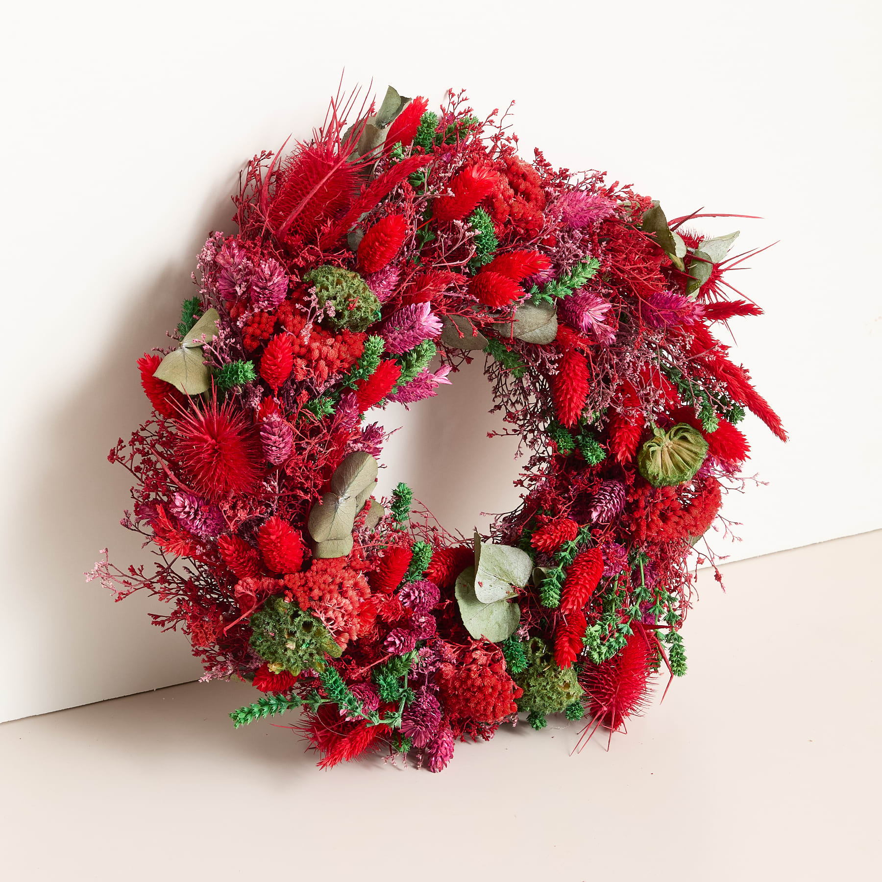 Auf einer schlichten, hellen Oberfläche befindet sich ein leuchtend rotes Blumenarrangement aus verschiedenen Blüten und Blättern.