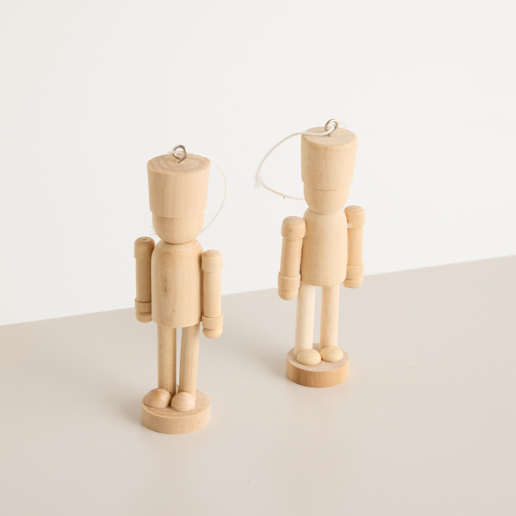 Aus einer weißen Vase wachsen kahle Zweige mit Knospen. An einem der Zweige hängt vor einem schlichten weißen Hintergrund eine kleine Holzfigur.