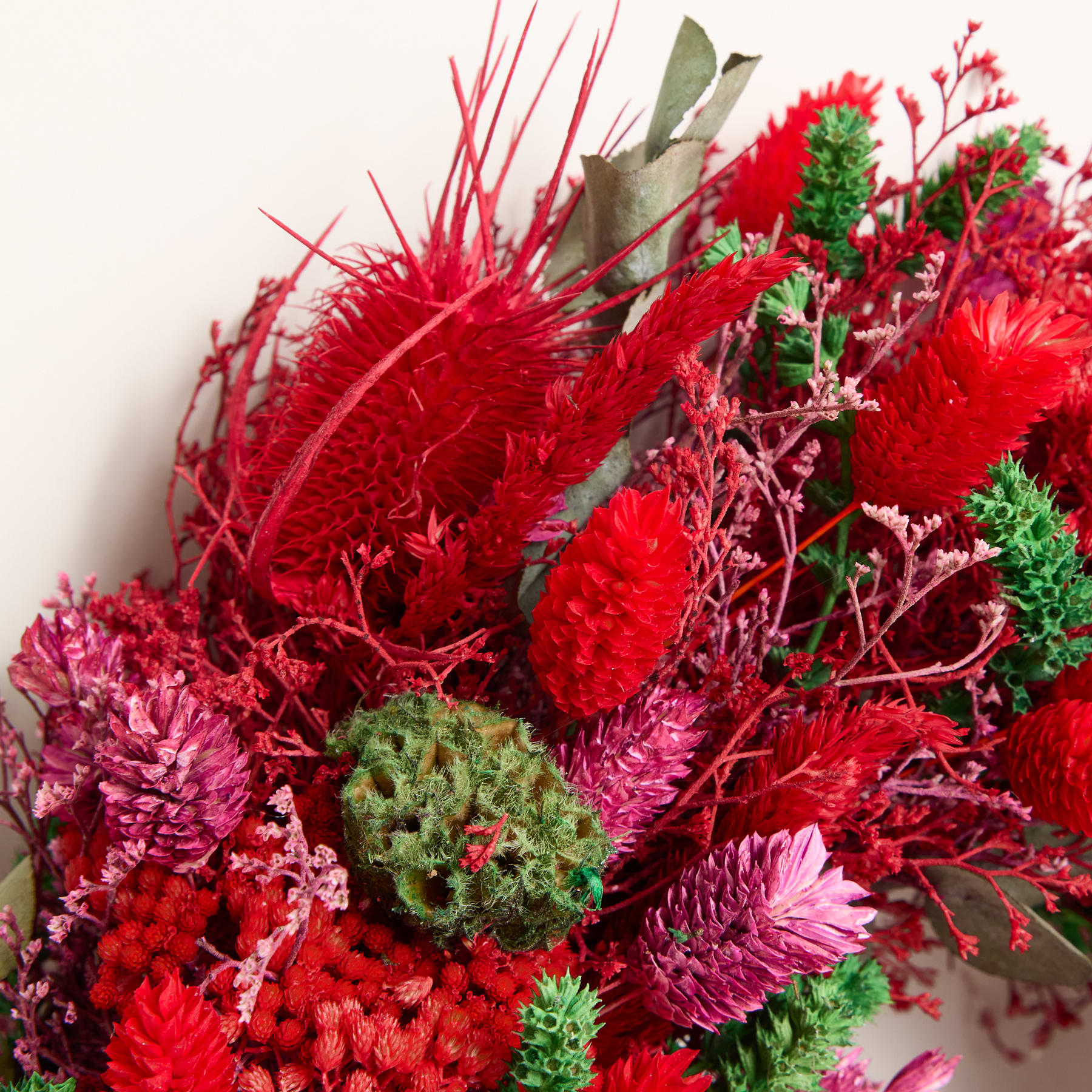 Ein lebendiger Strauß üppiger, karmesinroter Blumen und Blätter mit komplizierten Texturen und Formen vor einem neutralen Hintergrund.