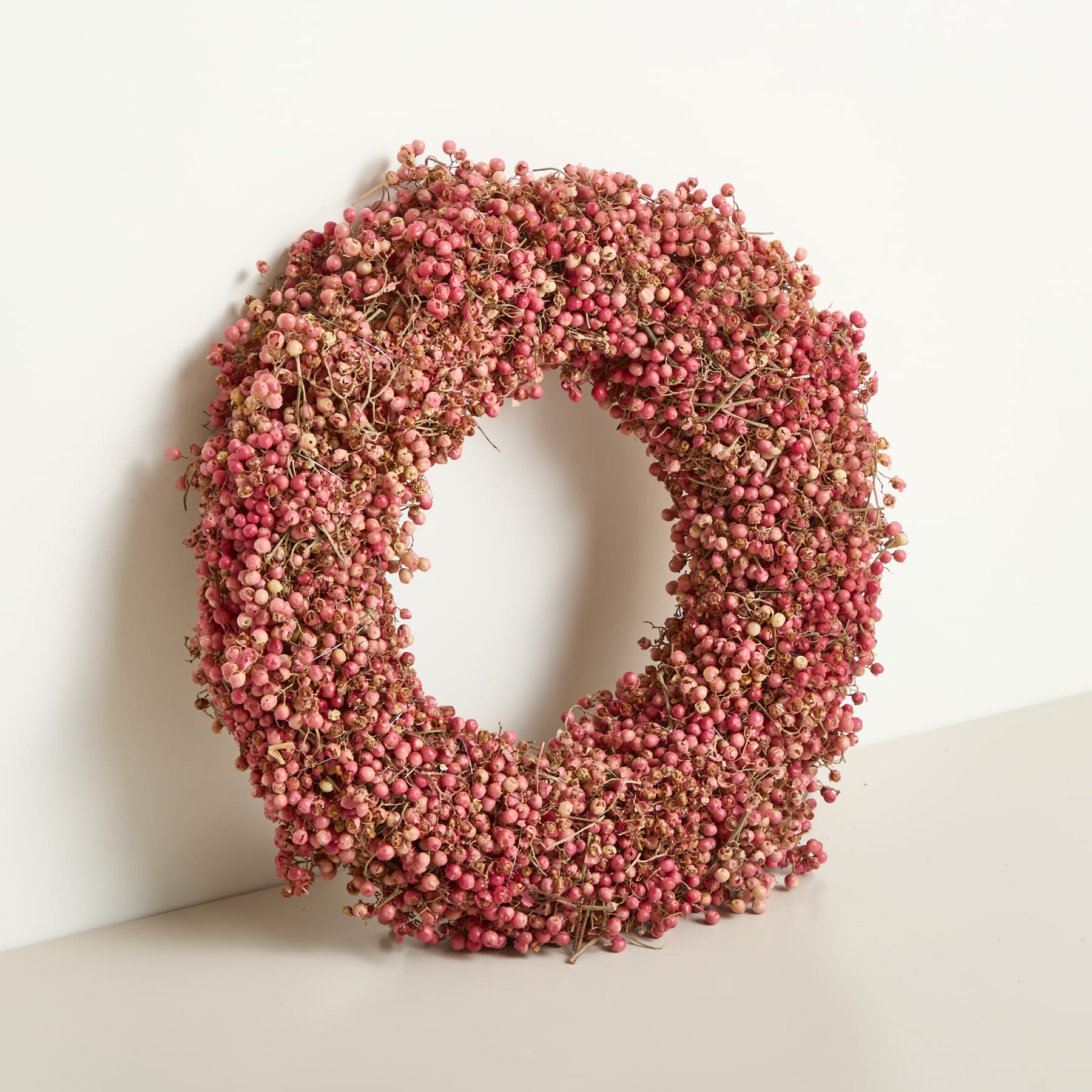 Ein Haufen leuchtend rötlich-rosa Pfefferkörner liegt auf einer schlichten, hellen Oberfläche.