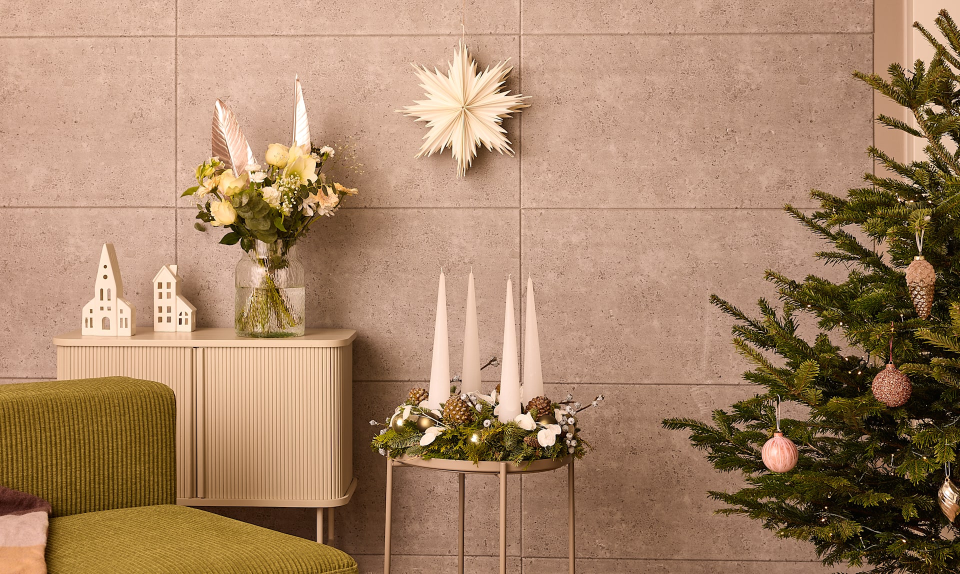 Ein gemütliches und festliches Wohnzimmerambiente mit einem geschmückten Weihnachtsbaum, Blumenarrangements und verschiedenen Weihnachtsdekorelementen vor einer neutral gefliesten Wand.