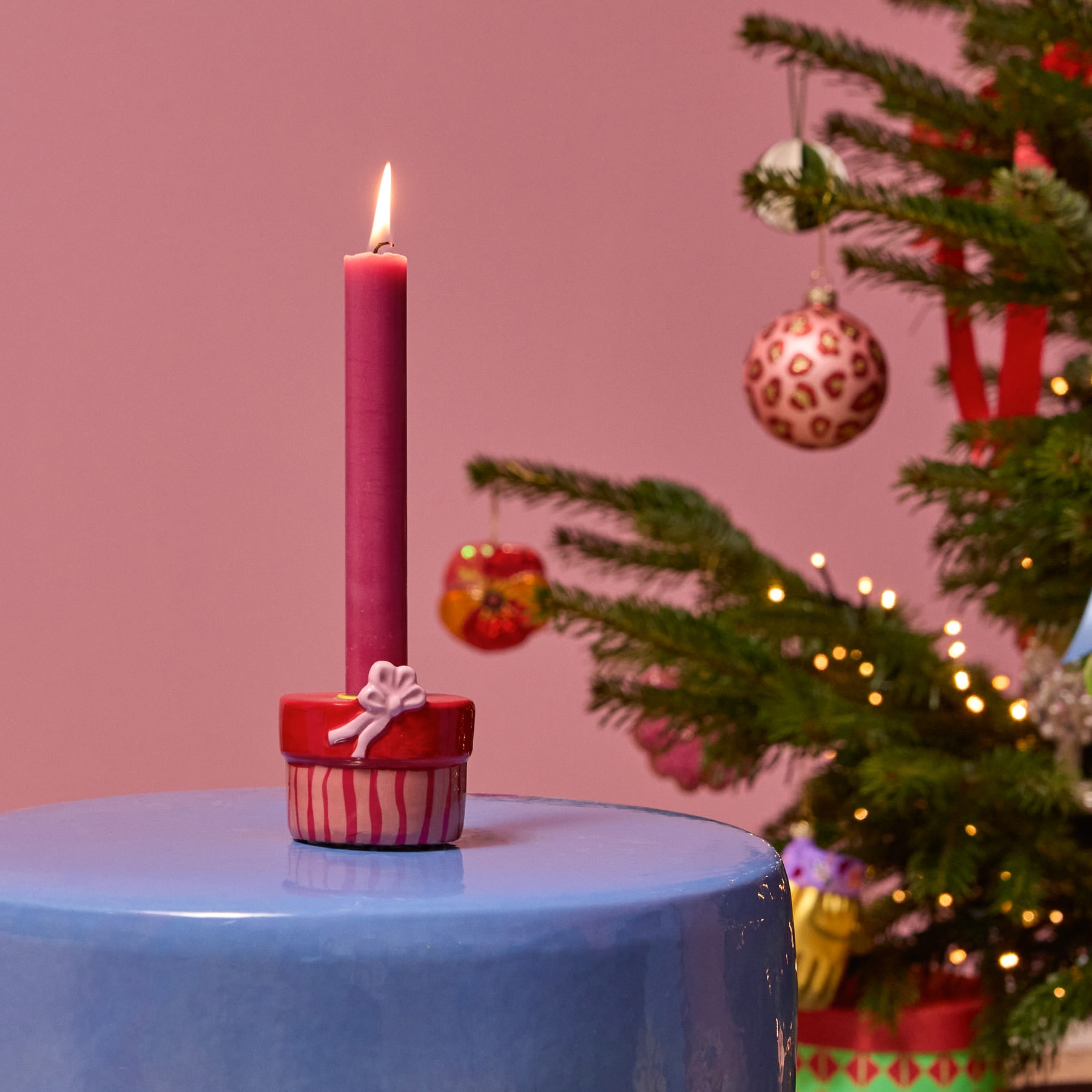 Ein roter, zylindrischer Kerzenhalter mit einer weißen Kerze steht auf einer hellen Fläche vor einem schlichten Hintergrund.