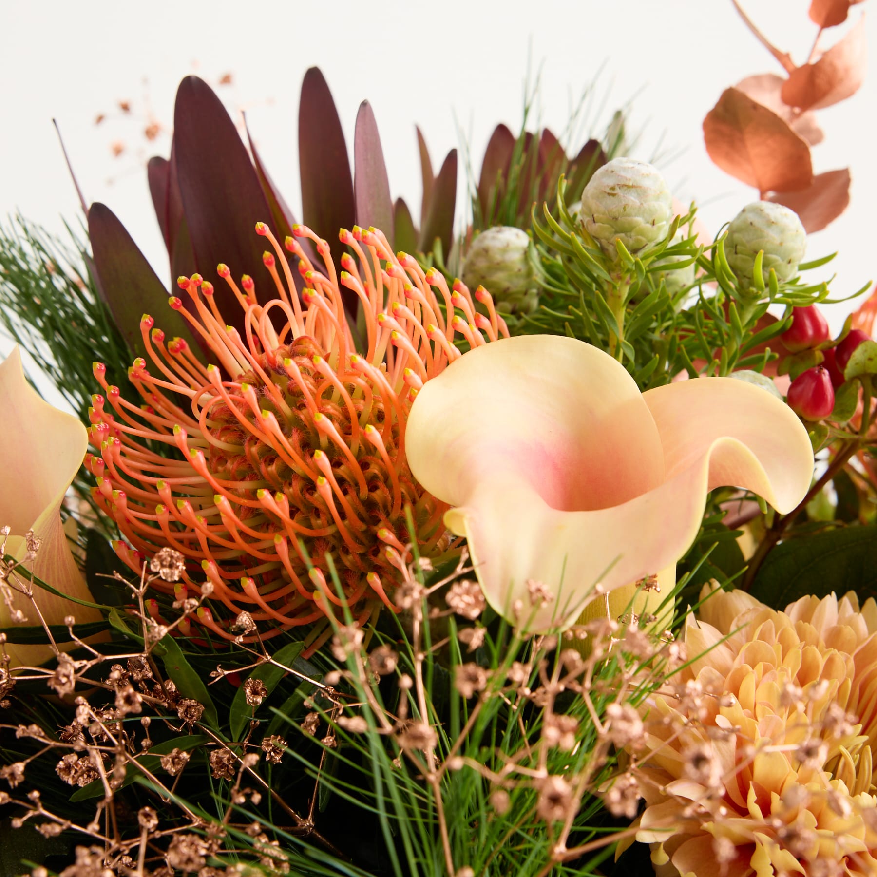 Ein lebendiger Strauß aus verschiedenen farbenfrohen Blumen, darunter Proteen, Calla-Lilien und üppiges Grün, der ein optisch beeindruckendes und fesselndes Arrangement ergibt.