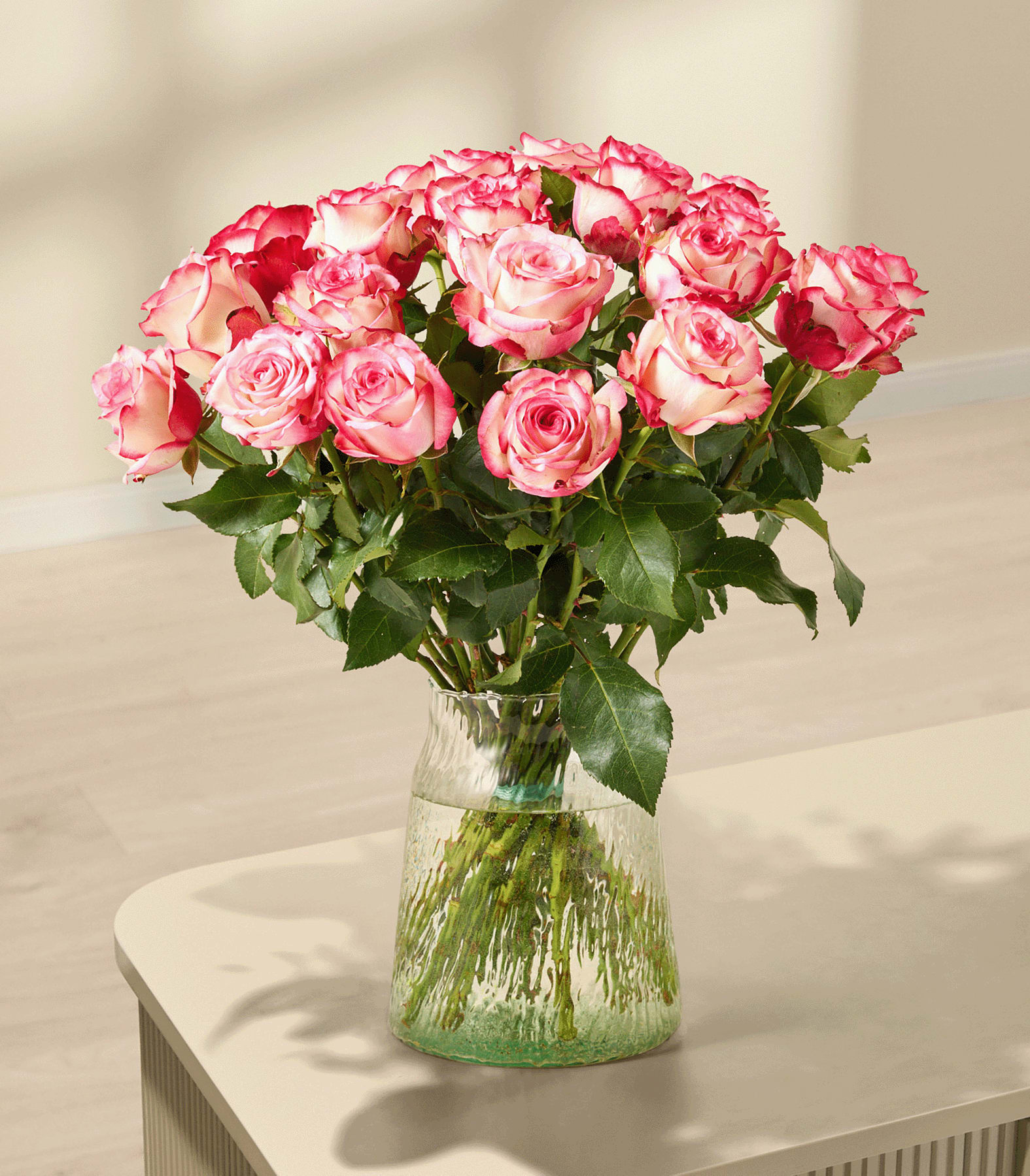 Ein Strauß leuchtend rosa Rosen, den eine Person vor einem schlichten weißen Hintergrund in den Händen hält.