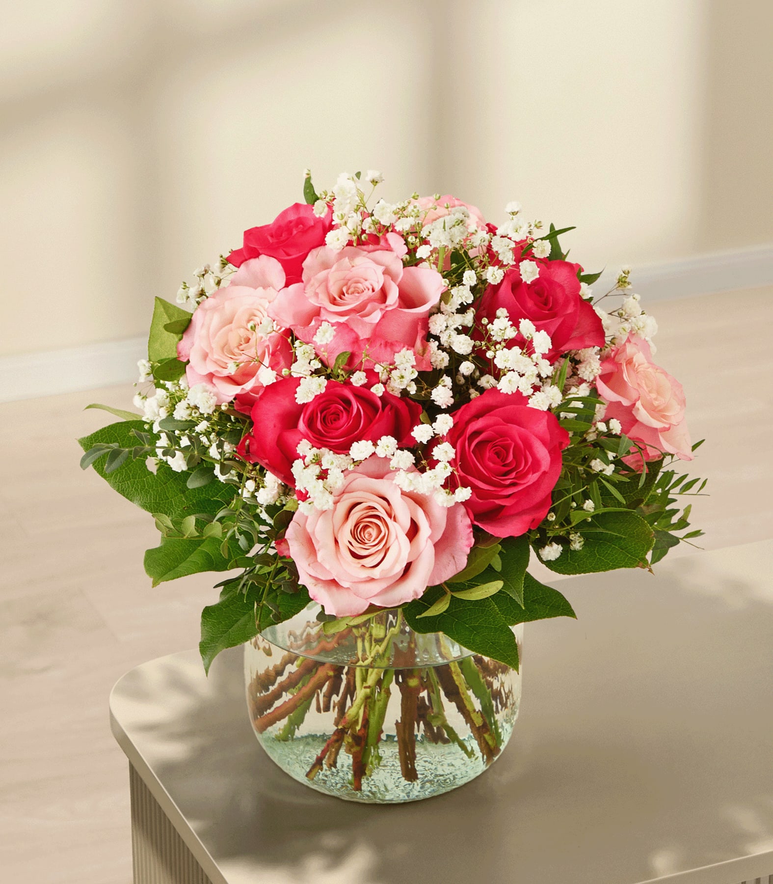 Ein leuchtender Strauß rosa und roter Rosen, umgeben von Grün, in den Händen einer Person vor einem schlichten weißen Hintergrund.