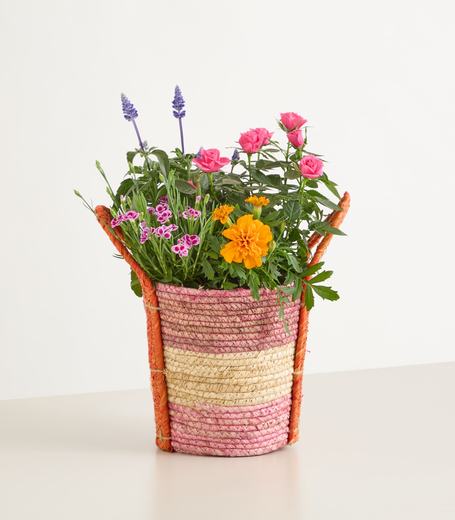 Ein bunter Strauß verschiedener Blumen, darunter Rosen, Lavendel und Ringelblumen, wird in einem geflochtenen Korb mit Streifenmuster präsentiert.