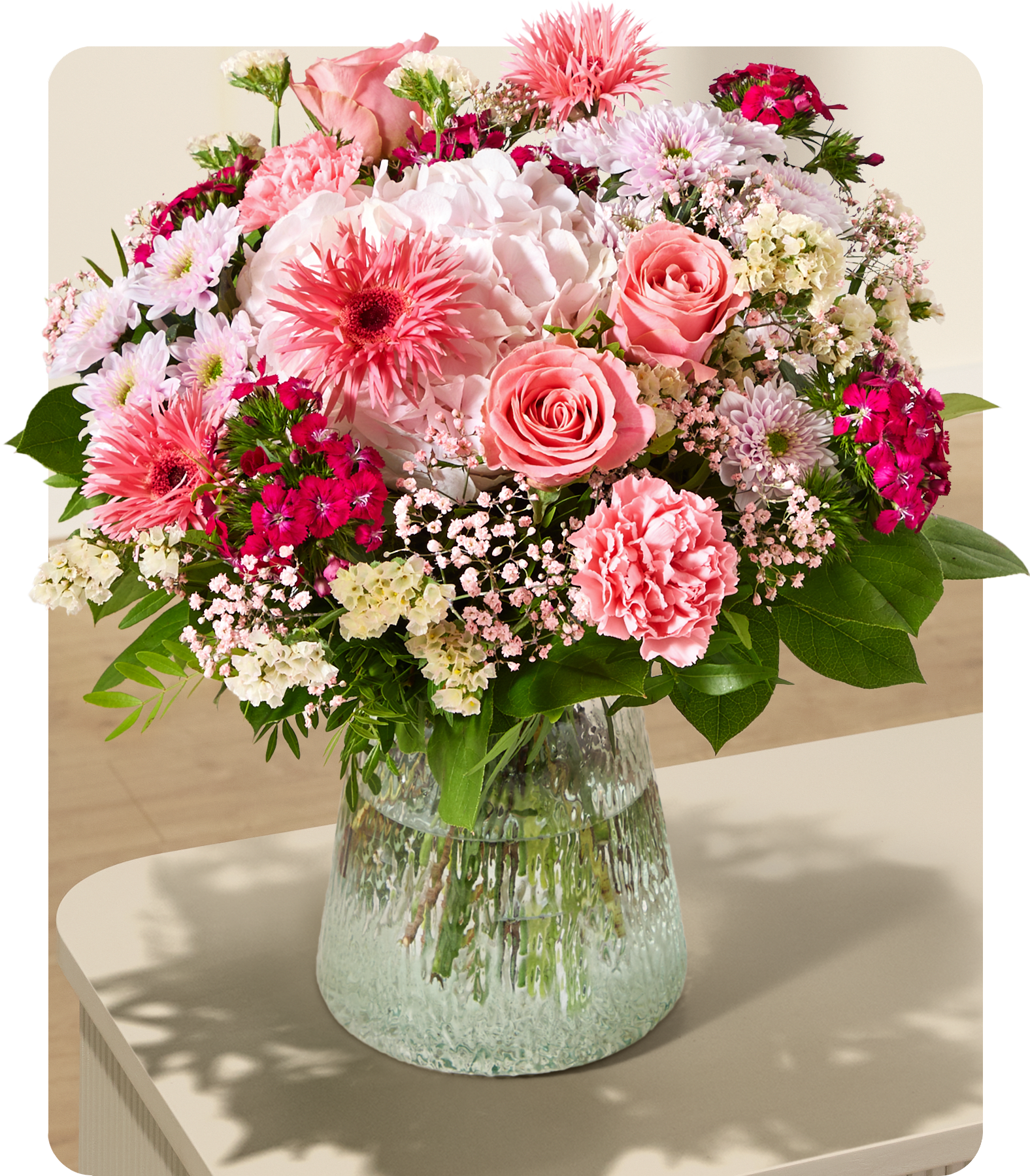 Im Vordergrund füllt ein lebhafter Strauß rosa und weißer Blumen eine strukturierte Glasvase vor einem sanft verschwommenen, hellen Hintergrund.