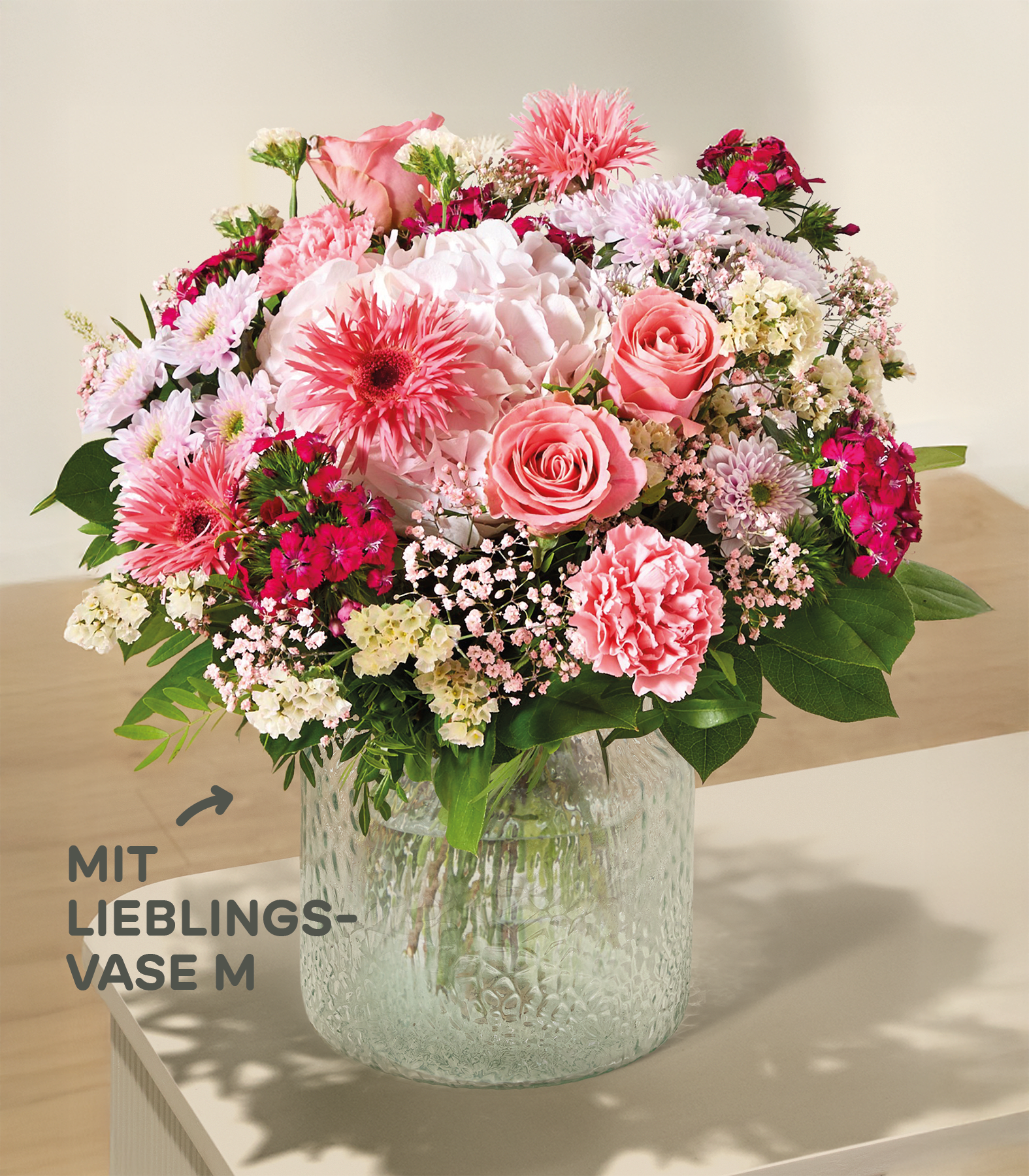 Im Vordergrund füllt ein lebhafter Strauß rosa und weißer Blumen eine strukturierte Glasvase vor einem sanften, neutralen Hintergrund.