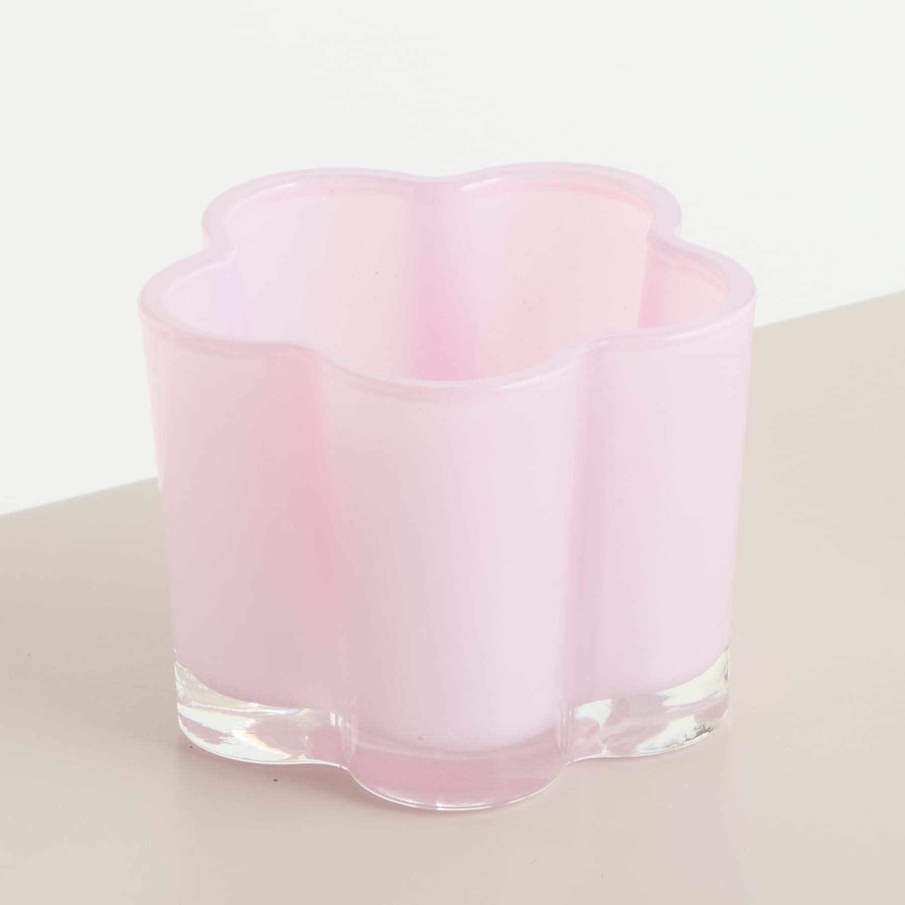 Eine zarte, rosafarbene Glasvase mit blumenähnlicher Form steht auf einer hellen Oberfläche.