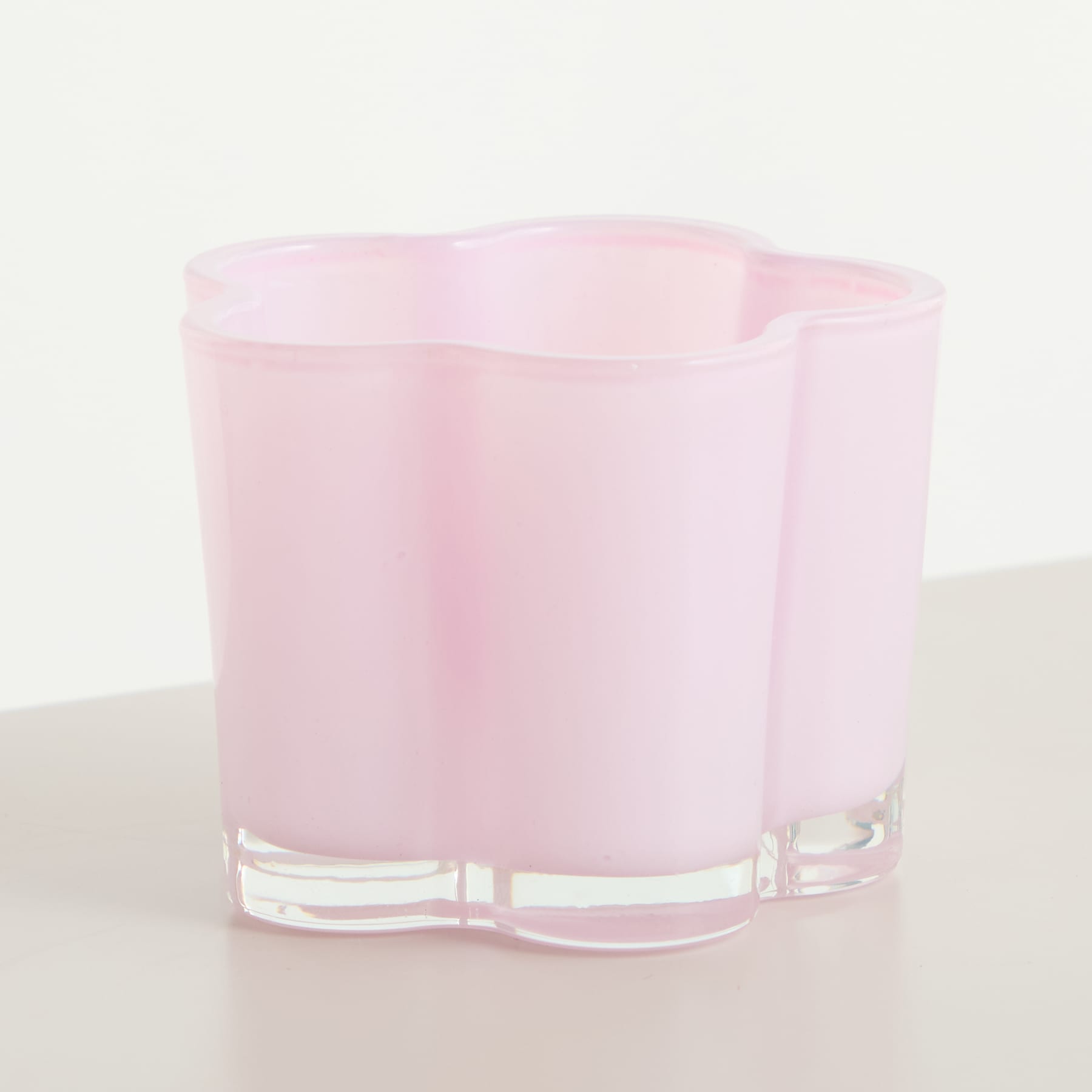 Auf einer hellen Oberfläche steht ein rosafarbener Glasbehälter mit gewelltem, gezacktem Rand.
