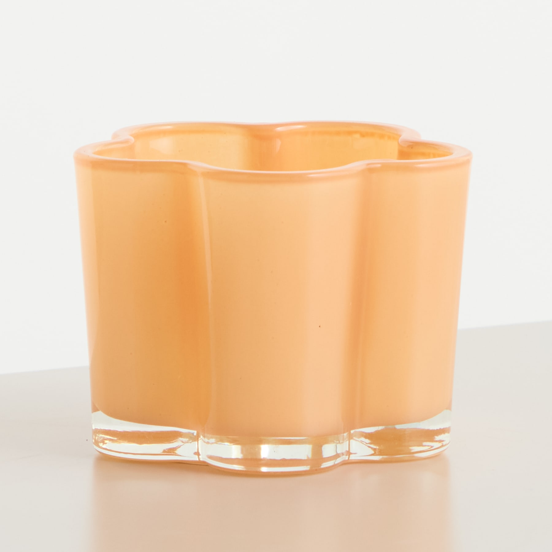 Auf einer hellen Oberfläche steht ein pfirsichfarbener Glasbehälter mit gewelltem, gezacktem Rand.
