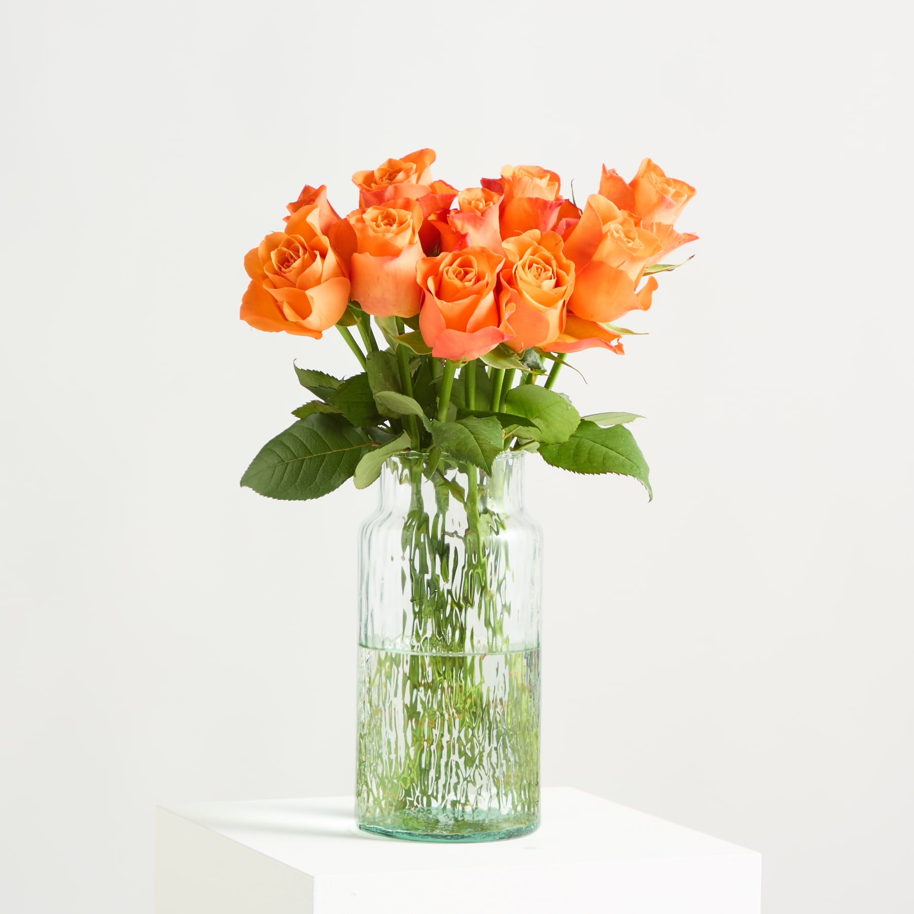 Leuchtend orangefarbene Rosen mit üppigen Blütenblättern und grünen Blättern füllen den Rahmen und ergeben ein auffälliges und optisch ansprechendes Blumenarrangement.