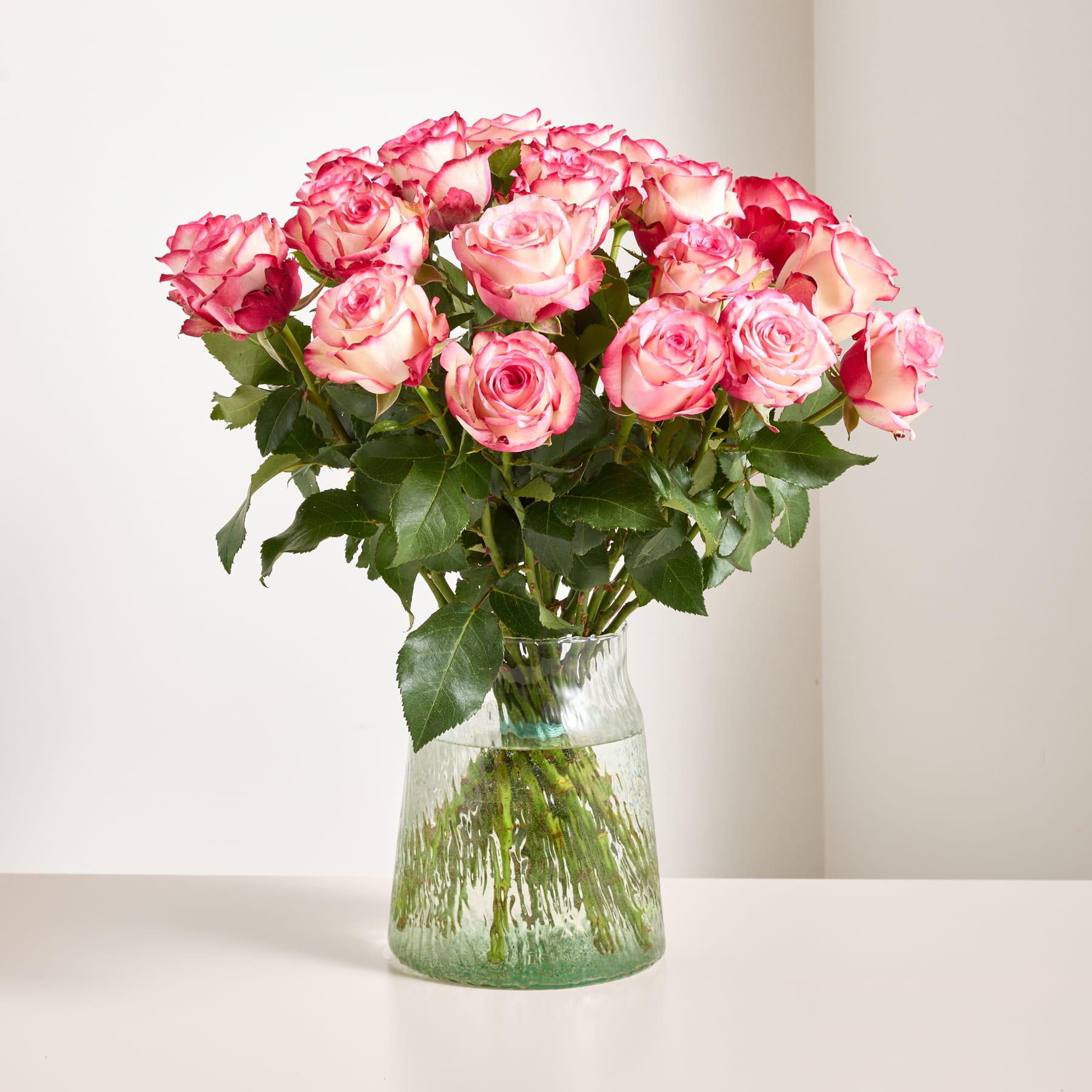 Ein Strauß leuchtend rosa Rosen, den eine Person vor einem schlichten weißen Hintergrund in den Händen hält.