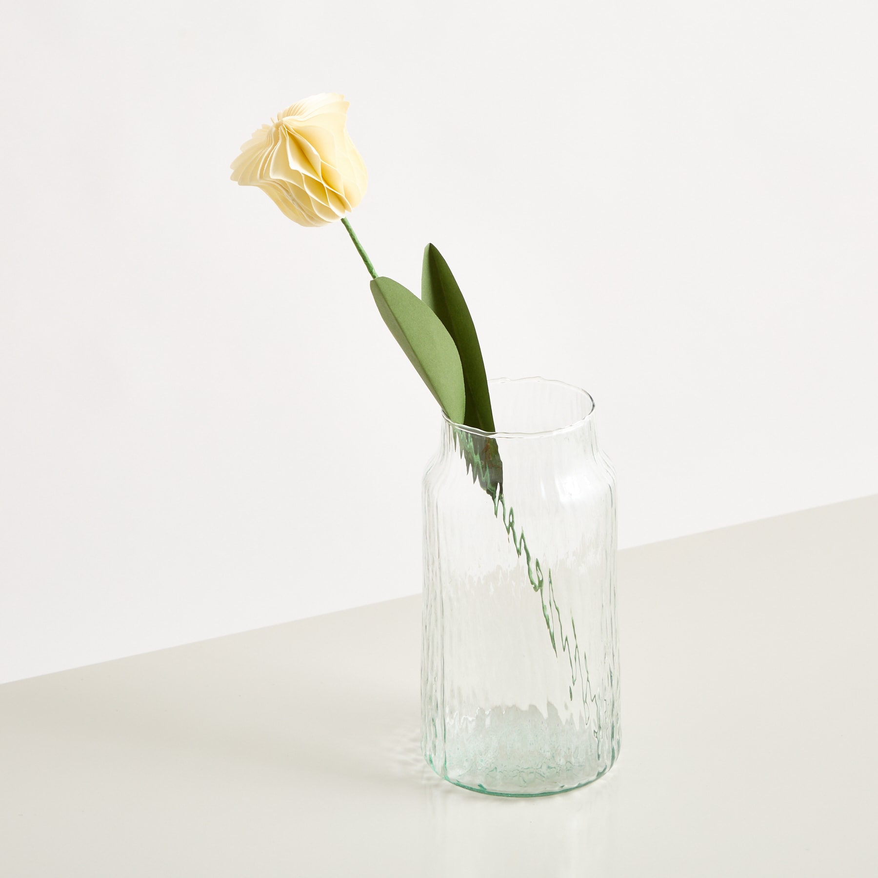 Eine einzelne gelbe Rose steht in einer durchsichtigen Glasvase vor einem schlichten weißen Hintergrund.