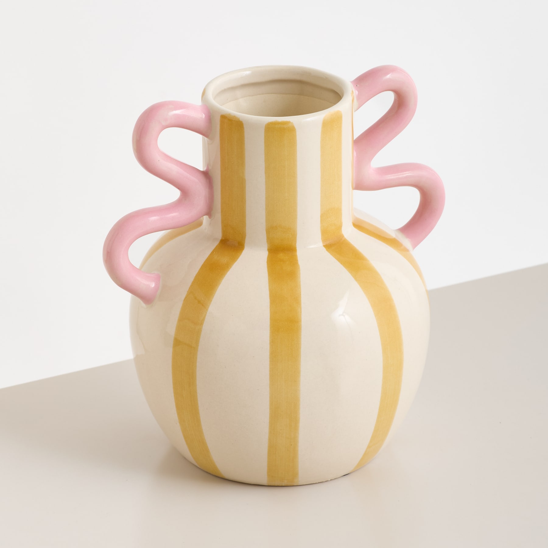 Eine Keramikvase mit einem einzigartigen, verspielten Design mit rosa Henkeln und gelben Streifen auf weißem Grund.