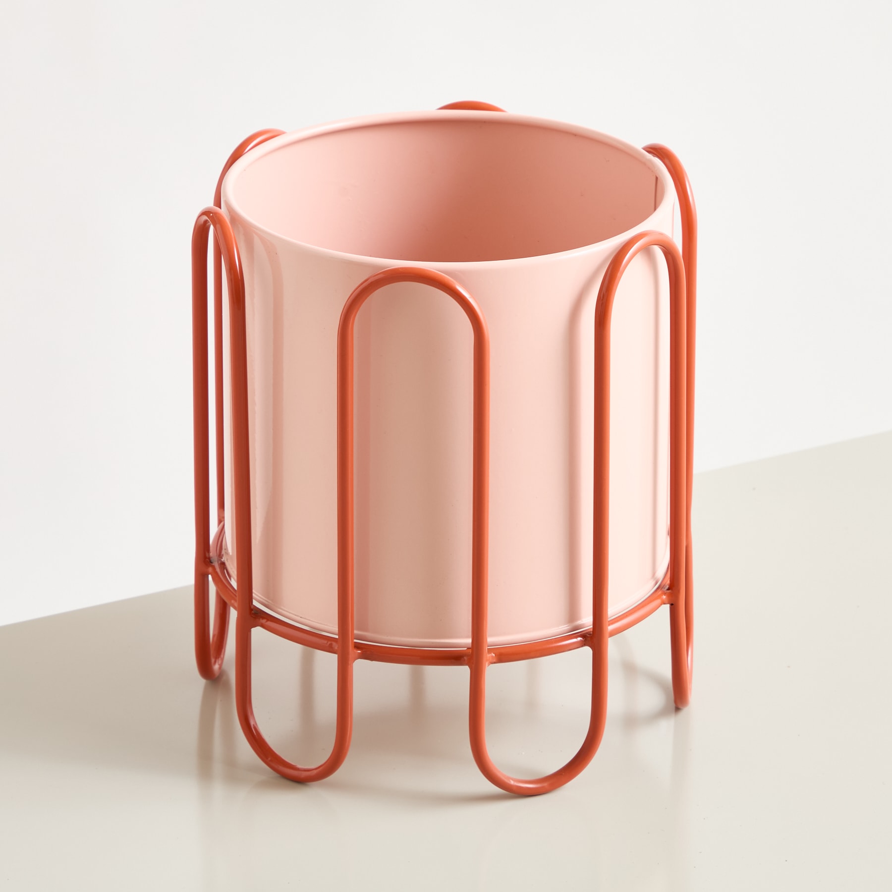 Ein rosafarbener Keramik-Pflanztopf oder eine Vase mit einzigartigem, minimalistischem Design, das sich durch geschwungene Metallgriffe vor einem schlichten weißen Hintergrund auszeichnet.