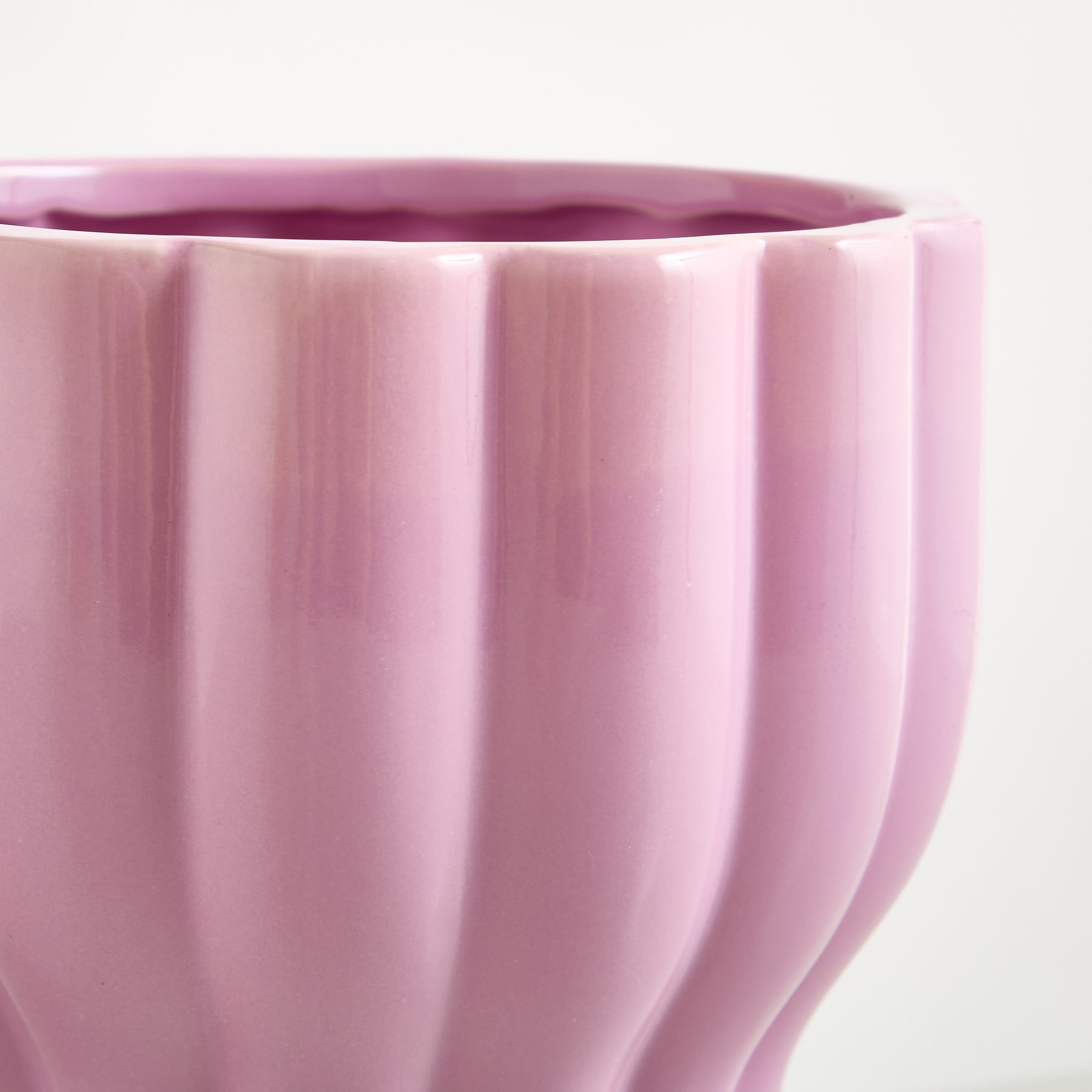 Eine leuchtend pinkfarbene Keramikvase mit einem einzigartigen, geriffelten Muster hebt sich deutlich von einem schlichten, weißen Hintergrund ab.