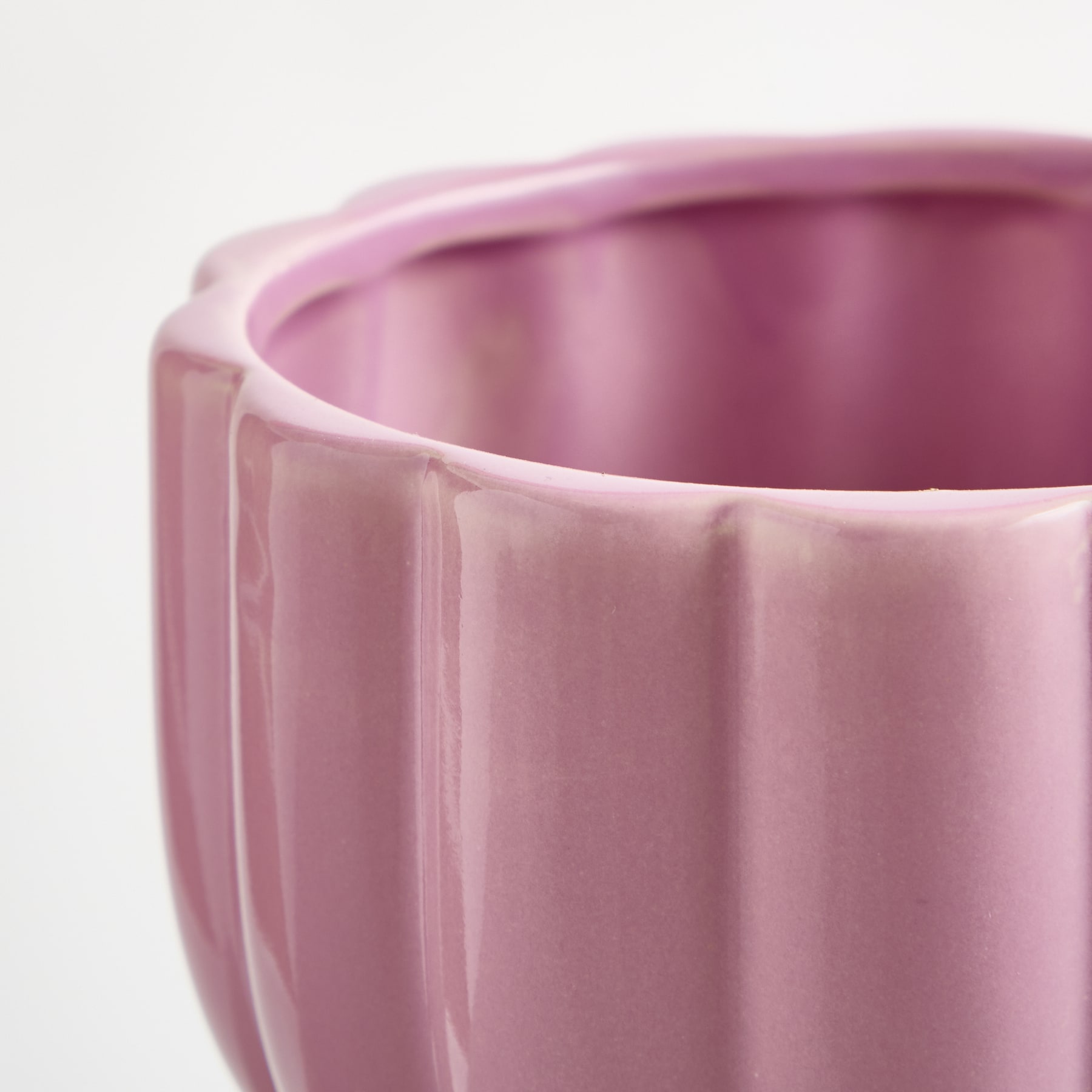 Nahaufnahme einer rosa Keramikvase mit strukturierter, gerippter Oberfläche vor einem schlichten weißen Hintergrund.