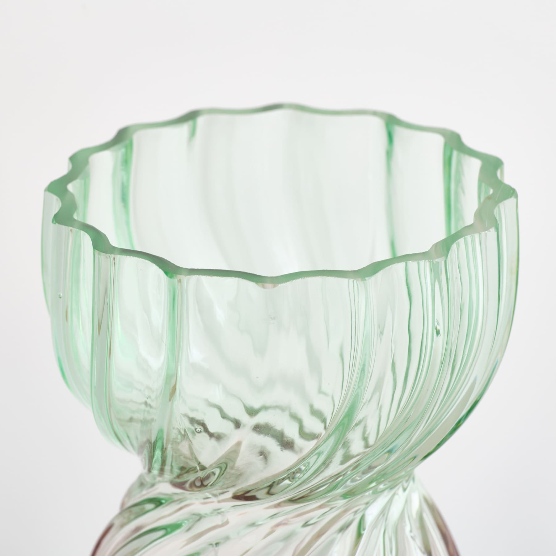 Eine durchsichtige grüne Glasschale mit gewelltem Rand steht auf einem schlichten weißen Hintergrund.