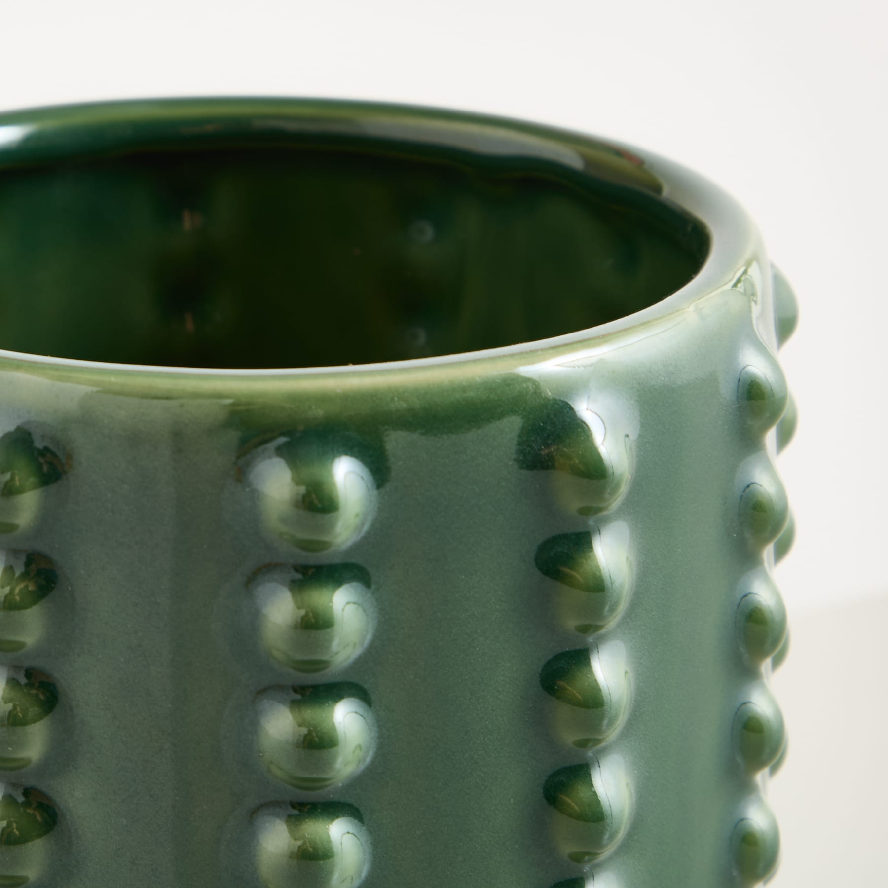 Eine grüne Keramiktasse mit strukturierter, unebener Oberfläche und glänzendem Finish vor einem schlichten Hintergrund.