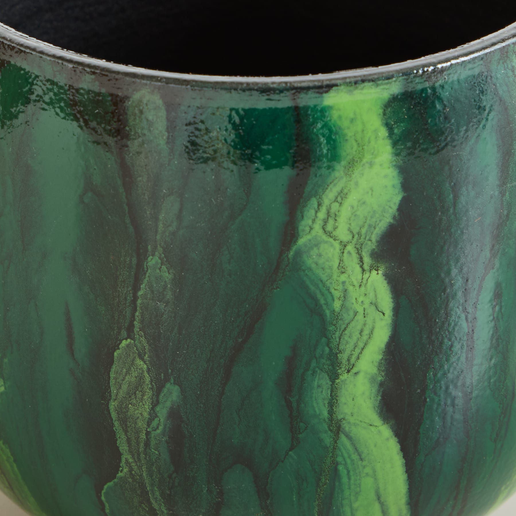 Das Bild zeigt eine Nahaufnahme eines Glas- oder Keramikgefäßes mit einem lebhaften grün-schwarzen Marmor- oder Wirbelmuster, das ein abstraktes und optisch beeindruckendes Erscheinungsbild erzeugt.
