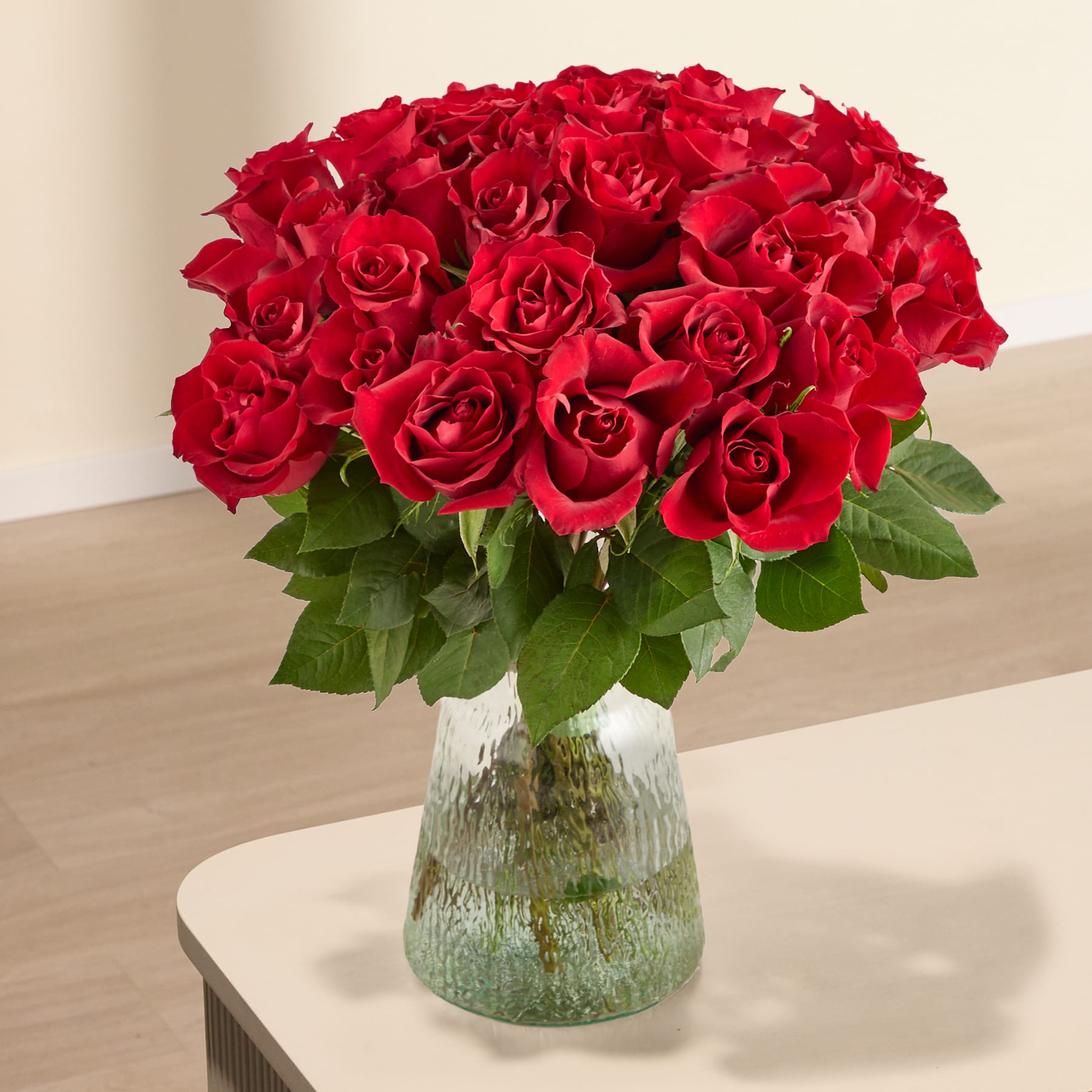 Ein großer Strauß leuchtend roter Rosen, den eine Person vor einem schlichten weißen Hintergrund in den Händen hält.