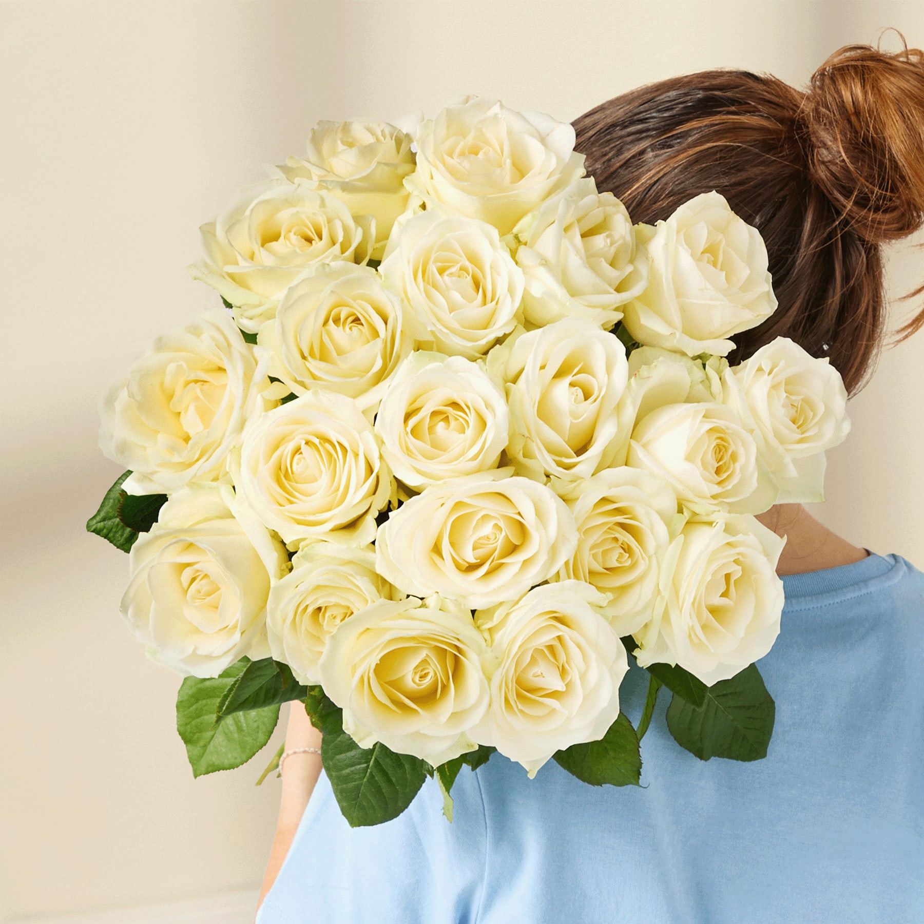 Eine Person in einem schwarzen Pullover hält einen Strauß wunderschöner weißer Rosen vor einem schlichten weißen Hintergrund.