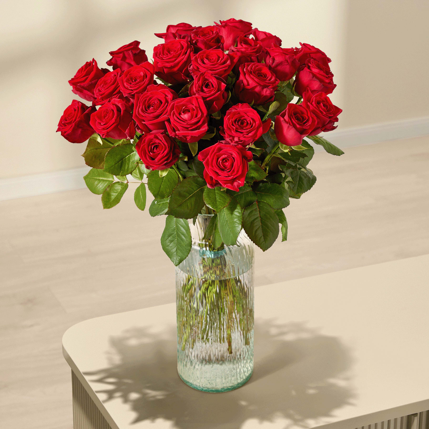 Ein großer Strauß leuchtend roter Rosen, den eine Person vor einem schlichten weißen Hintergrund in den Händen hält.