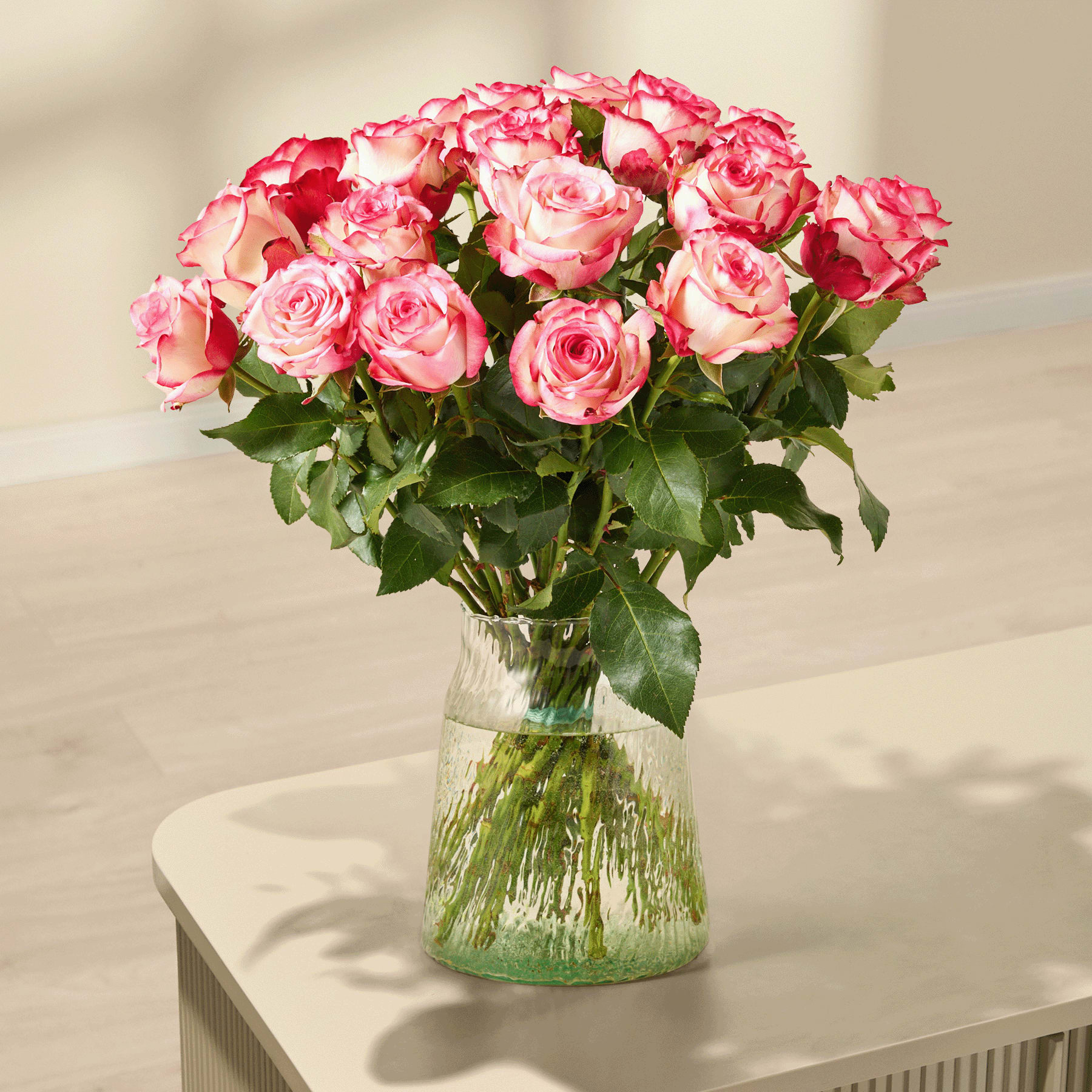 Ein Strauß leuchtend rosa Rosen, den eine Person vor einem schlichten weißen Hintergrund in den Händen hält.