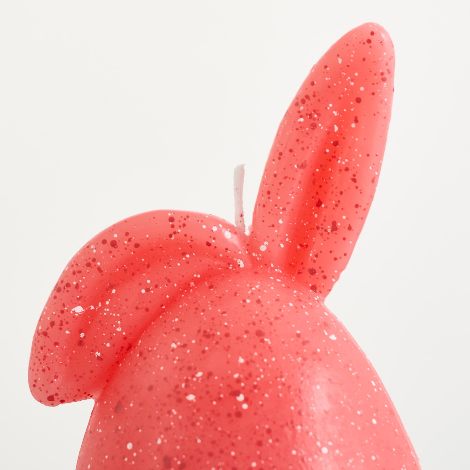 Ein weiches, pastellfarbenes, hasenförmiges Objekt liegt auf einer schlichten, hellen Oberfläche.