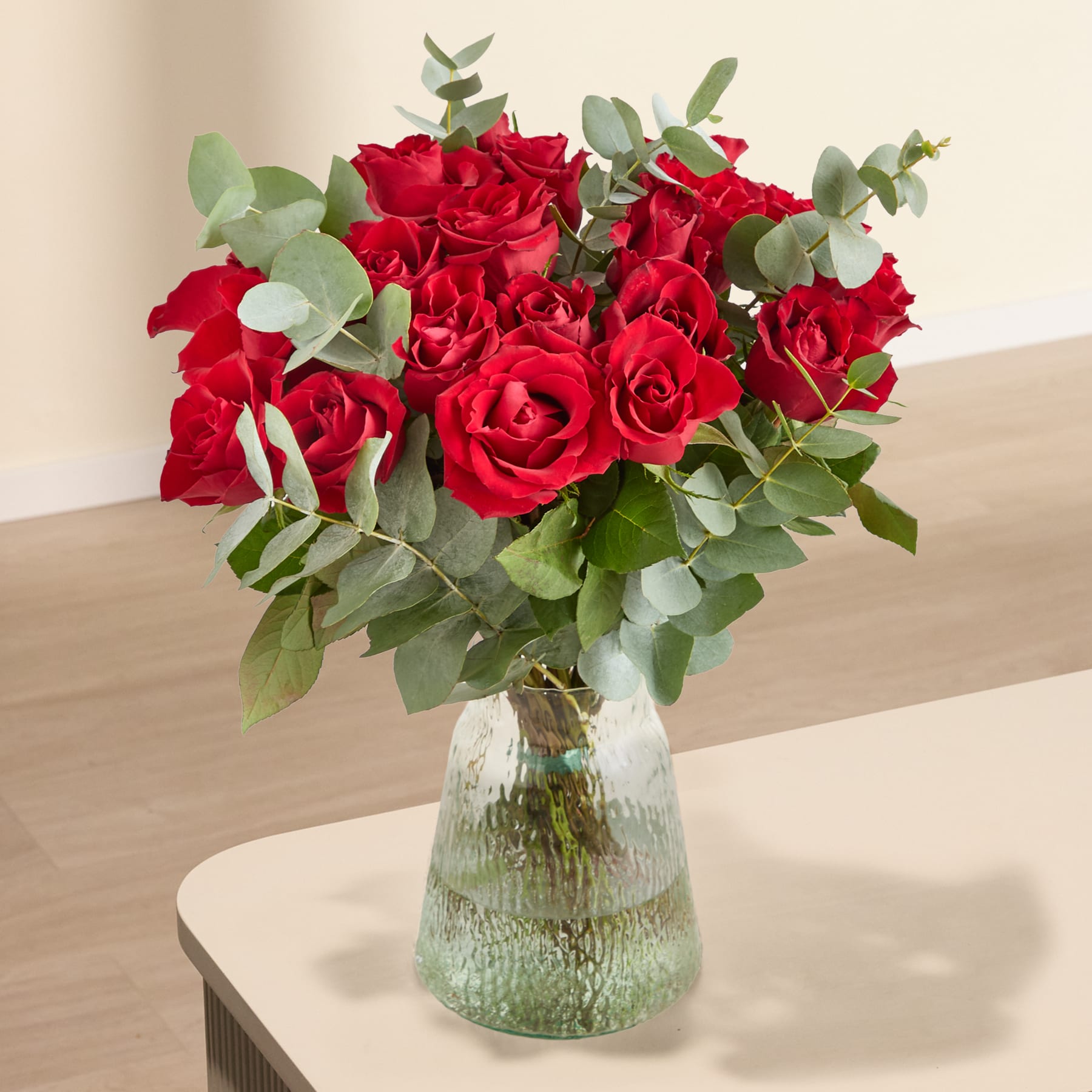 Ein großer Strauß leuchtend roter Rosen in den Händen einer Person vor einem schlichten weißen Hintergrund.