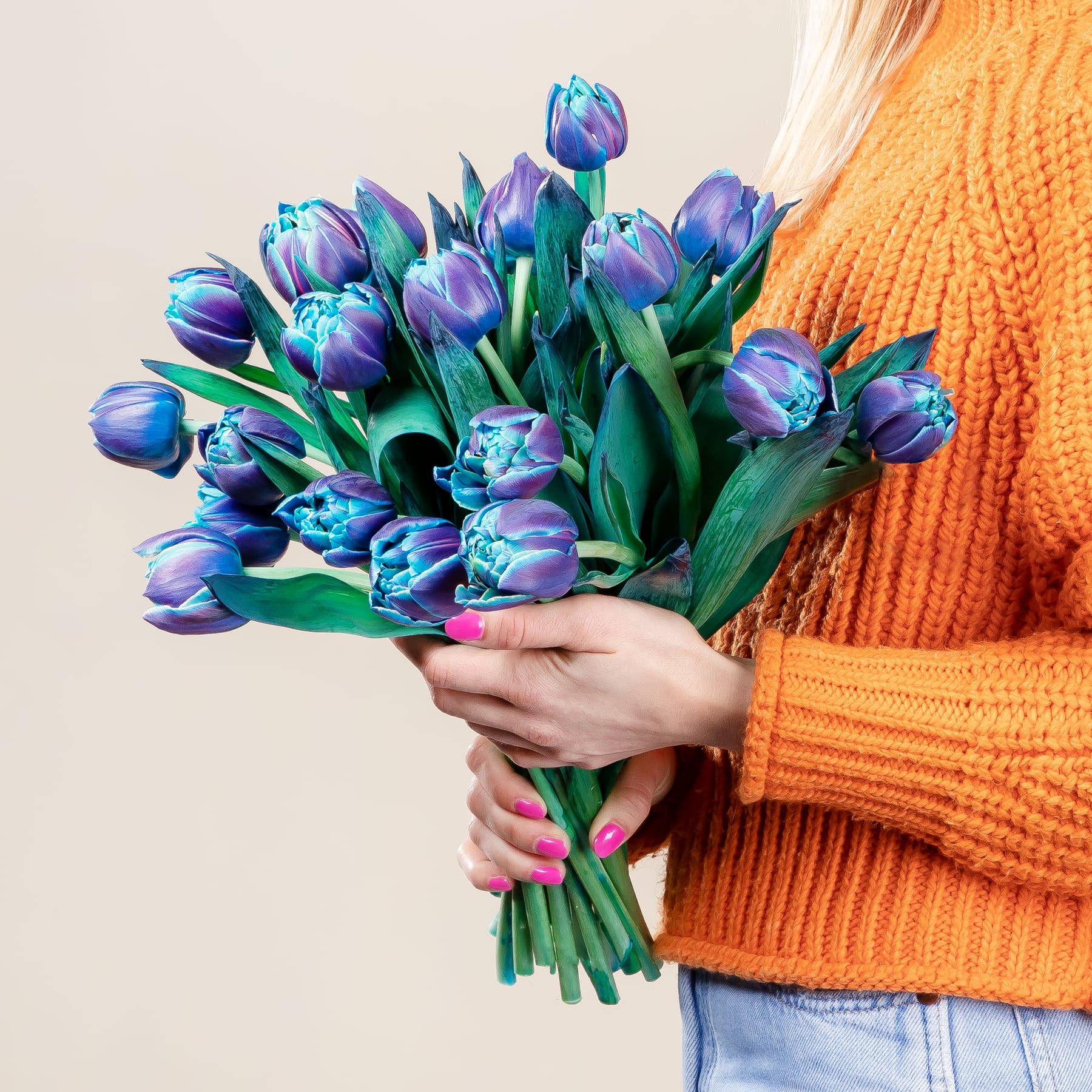 Eine einzelne, leuchtend grüne Tulpe in der Hand vor einem schlichten beigen Hintergrund.