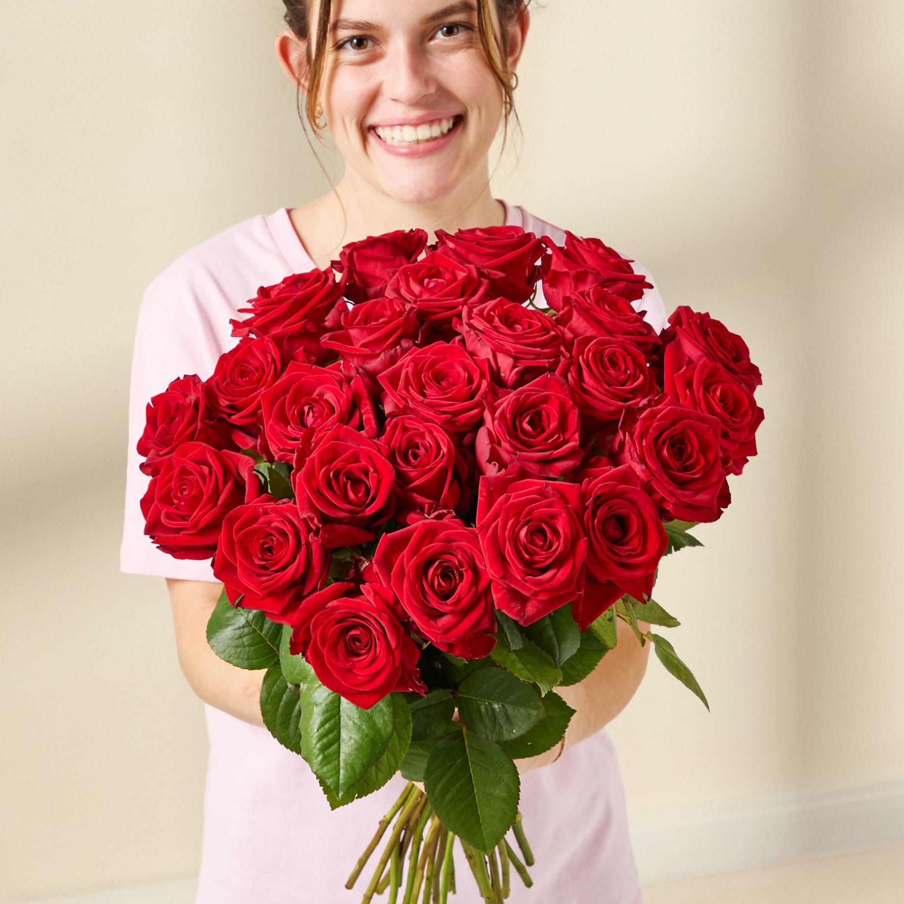 Ein Strauß leuchtend roter Rosen in einer Glasvase steht auf einer hellen Oberfläche vor einem schlichten Hintergrund.
