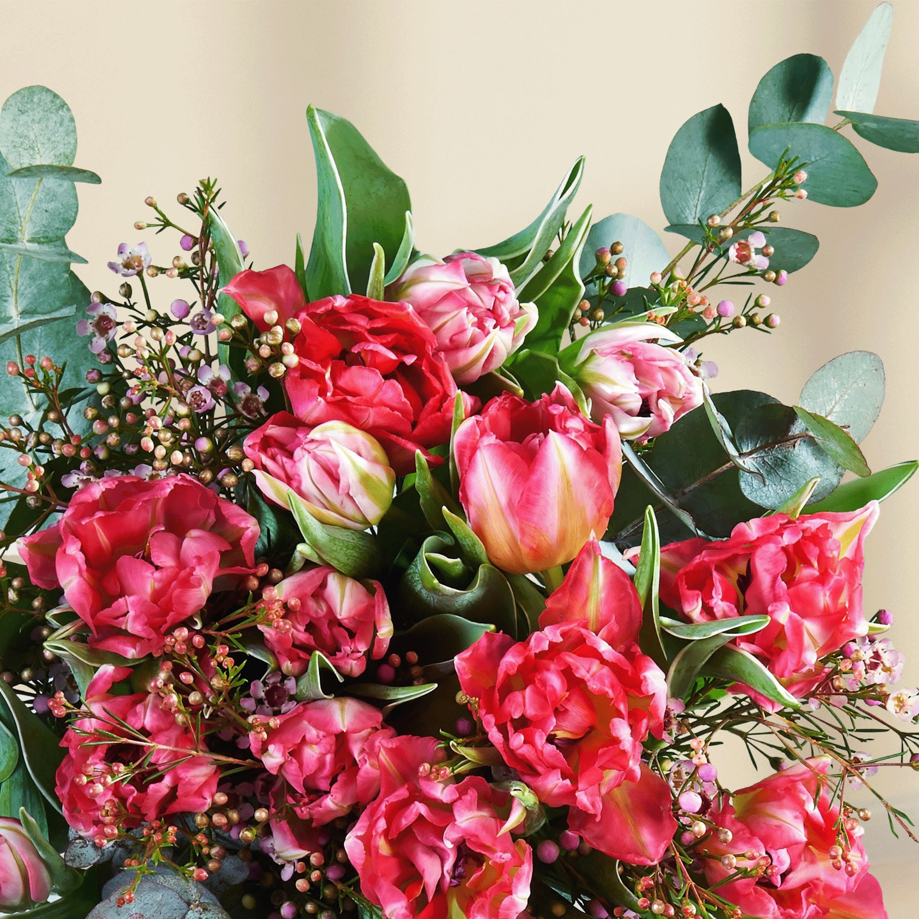 Ein leuchtender Strauß rosa und roter Blumen, darunter Tulpen, Pfingstrosen und andere Blüten, arrangiert vor einem schlichten weißen Hintergrund.