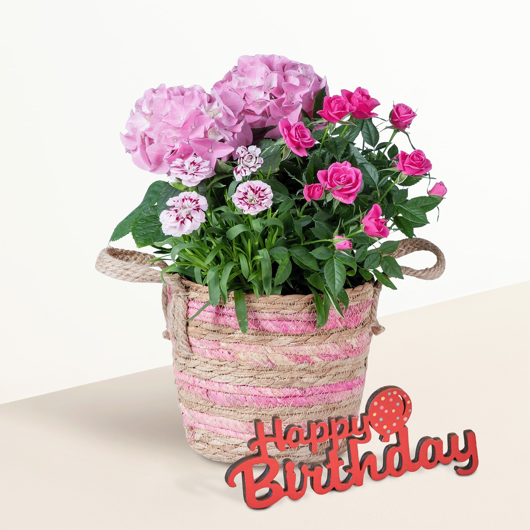 Ein leuchtender Strauß rosa Hortensien und Rosen in einem geflochtenen Korb vor einem schlichten, hellen Hintergrund.