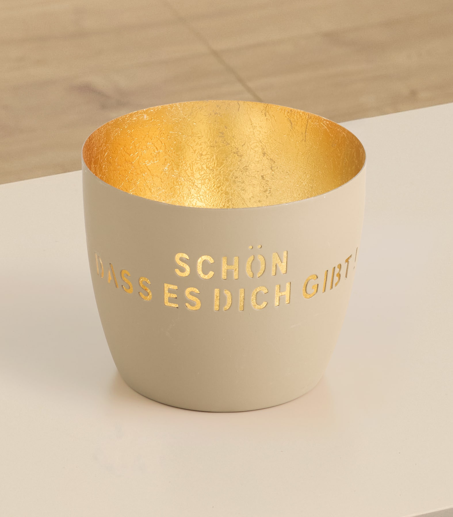 Eine beige Keramiktasse mit goldener Innenseite und dem in goldener Schrift aufgedruckten Text „Schon, dass es dich gibt“ auf der Außenseite.