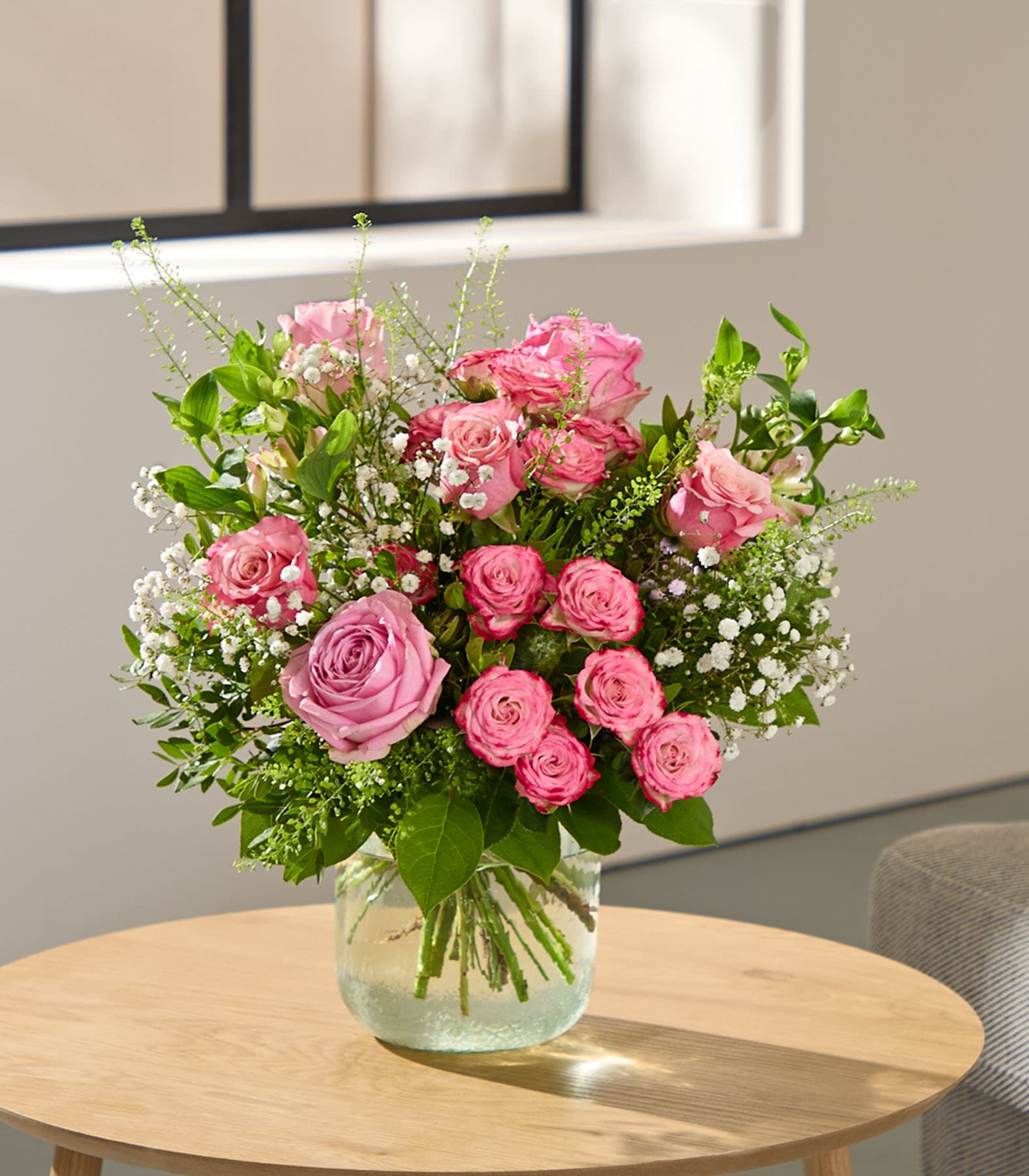 Ein Strauß leuchtend pinkfarbener Rosen und anderer zarter Blumen wird von einer Person in einem hellblauen Hemd vor einem verschwommenen Hintergrund gehalten.