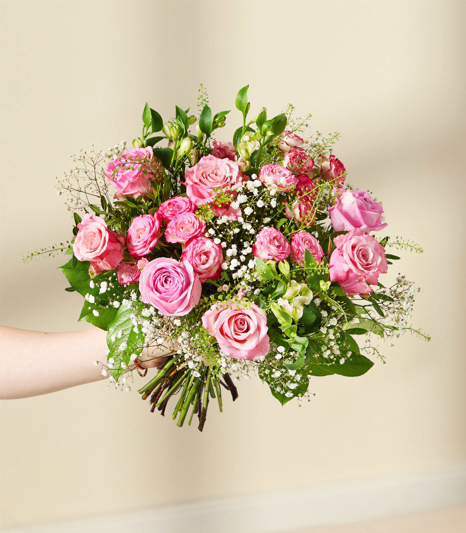 Ein leuchtender Strauß aus rosa und roten Rosen, umgeben von üppigem Grün und zartem Schleierkraut, vor einem schlichten, hellen Hintergrund.