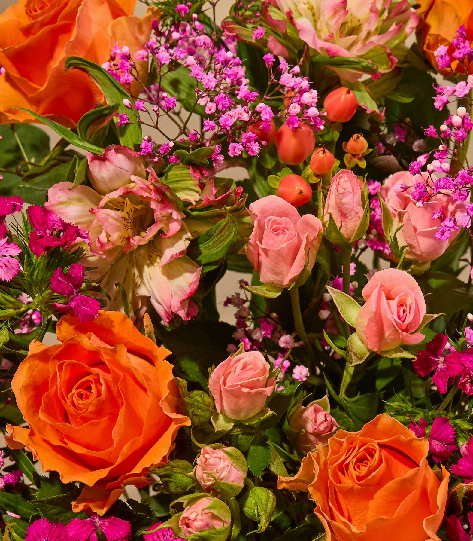 Ein farbenfroher Blumenstrauß mit Rosen, Dahlien und anderen Blüten wird von einer Person in einem schwarzen Hemd vor einem schlichten weißen Hintergrund gehalten.