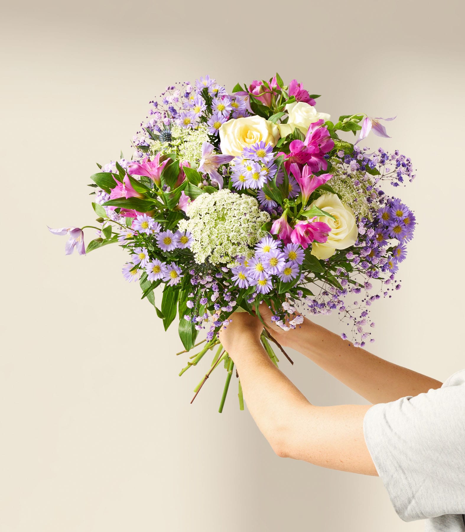 Ein lebendiger Strauß weißer Rosen, lila Chrysanthemen und anderer bunter Blumen, arrangiert in einer Glasvase vor einem schlichten weißen Hintergrund.