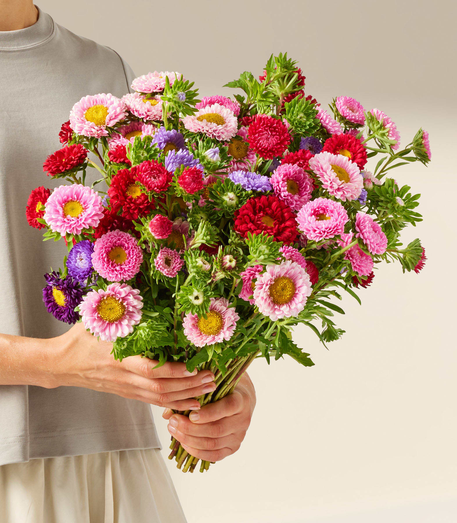 Ein farbenfroher Blumenstrauß, darunter rosa und rote Gänseblümchen, arrangiert in einer Glasvase vor schlichtem weißen Hintergrund.