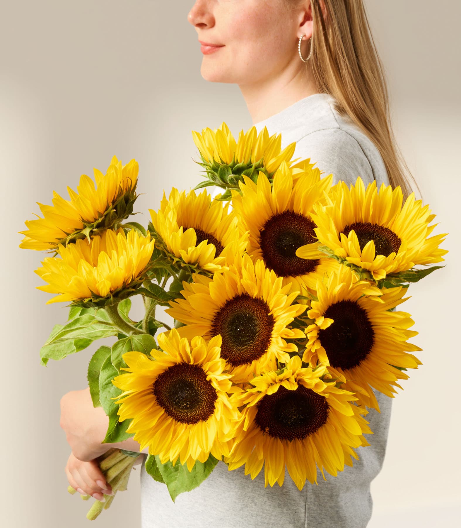 Eine junge Frau hält einen farbenfrohen Strauß gelber Sonnenblumen vor einem schlichten weißen Hintergrund.