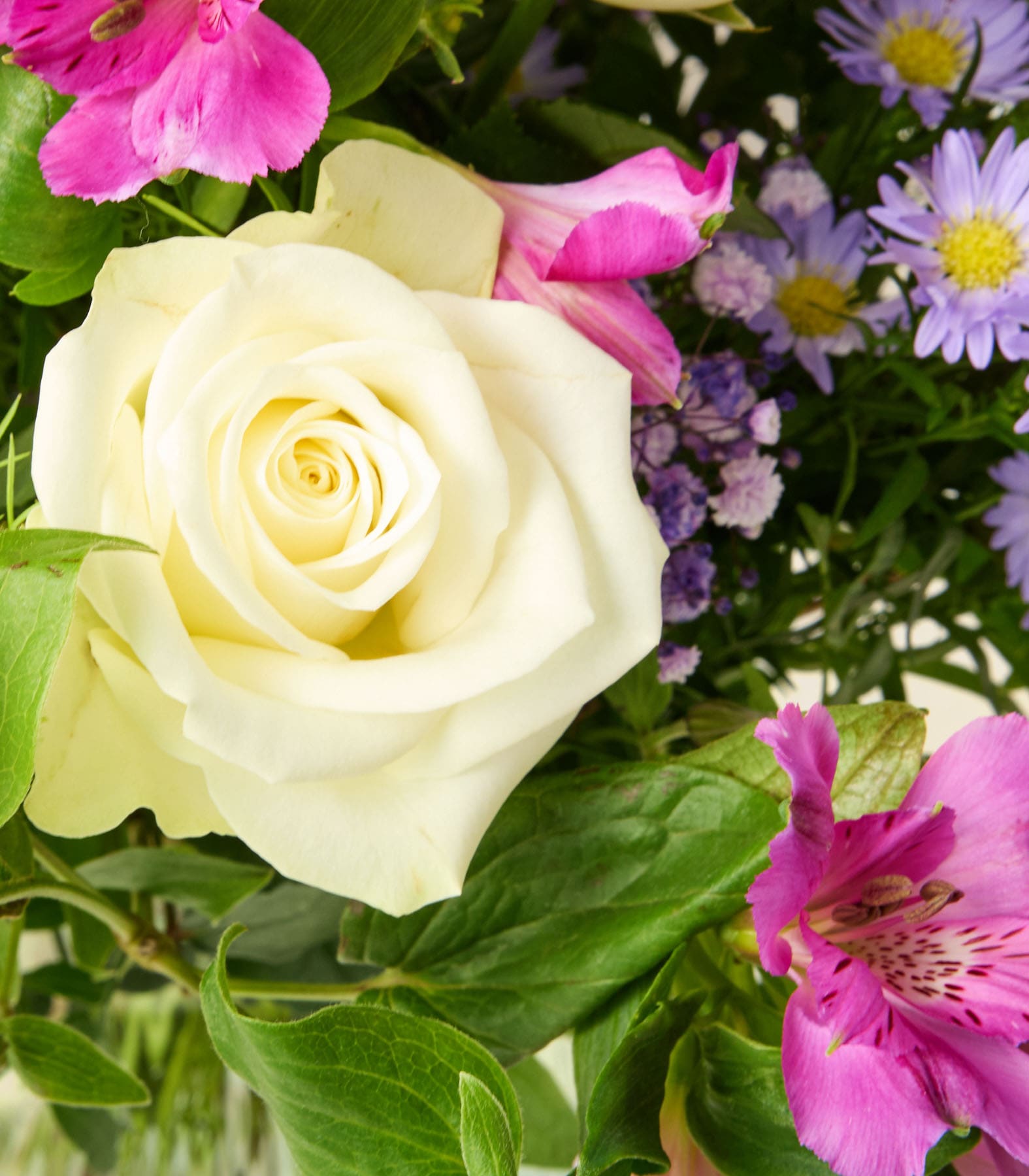Ein lebendiger Blumenstrauß, darunter eine wunderschöne gelbe Rose, rosa Inkalilien und violette Gänseblümchen, vor einem Hintergrund aus üppigem grünem Laub.