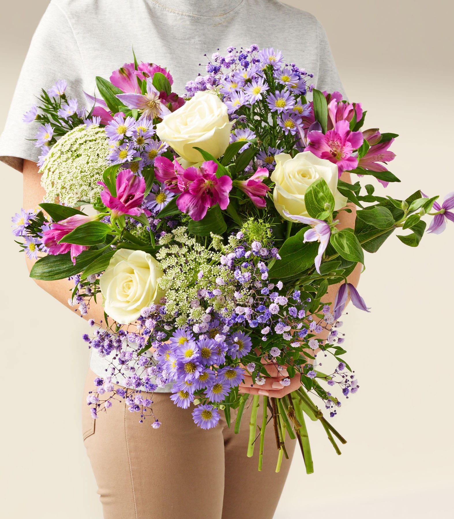 Ein lebendiger Strauß bunter Blumen, darunter Rosen, Gänseblümchen und andere Blüten, wird im Vordergrund vor einem schlichten weißen Hintergrund gehalten.