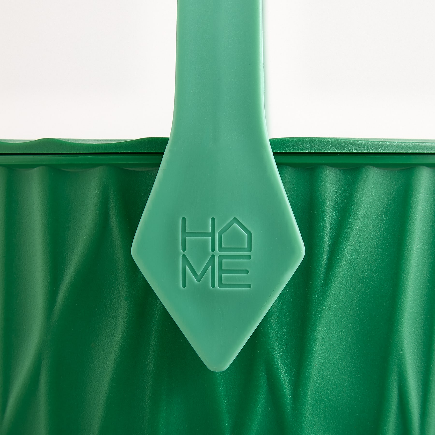 Vor weißem Hintergrund ist ein grüner Korb mit rautenförmigem Henkel und der Aufschrift „HOME“ abgebildet.